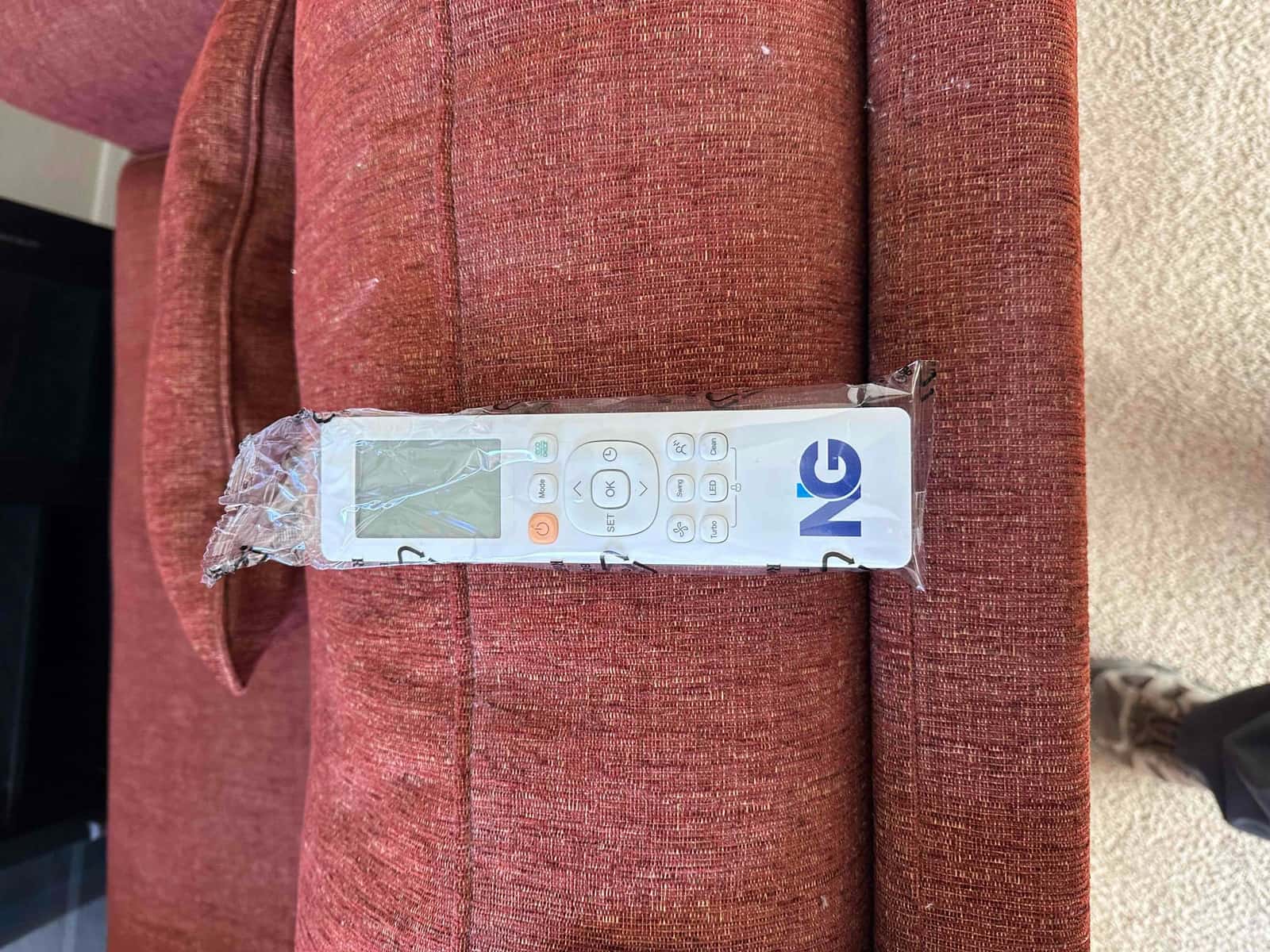 New mini-split handheld remote in protective plastic wrap placed on a sofa at the installation site.