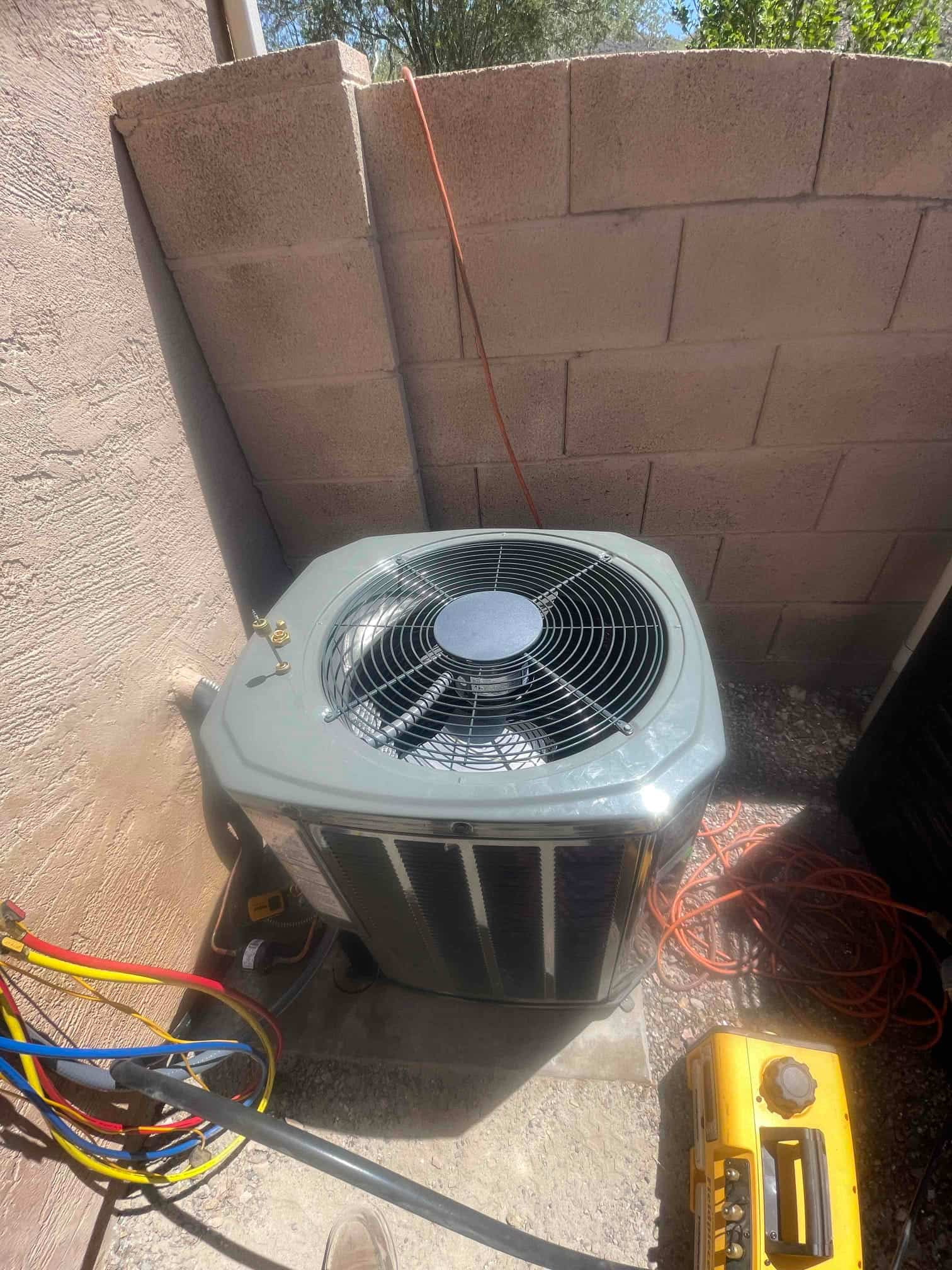 New outdoor condenser set on a concrete pad with connected refrigerant hoses and nearby service equipment during installation.