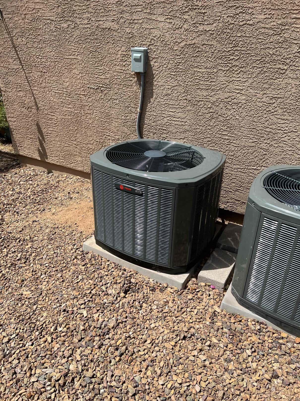 New outdoor condenser set on a level pad with electrical disconnect mounted on the wall and gravel base below.