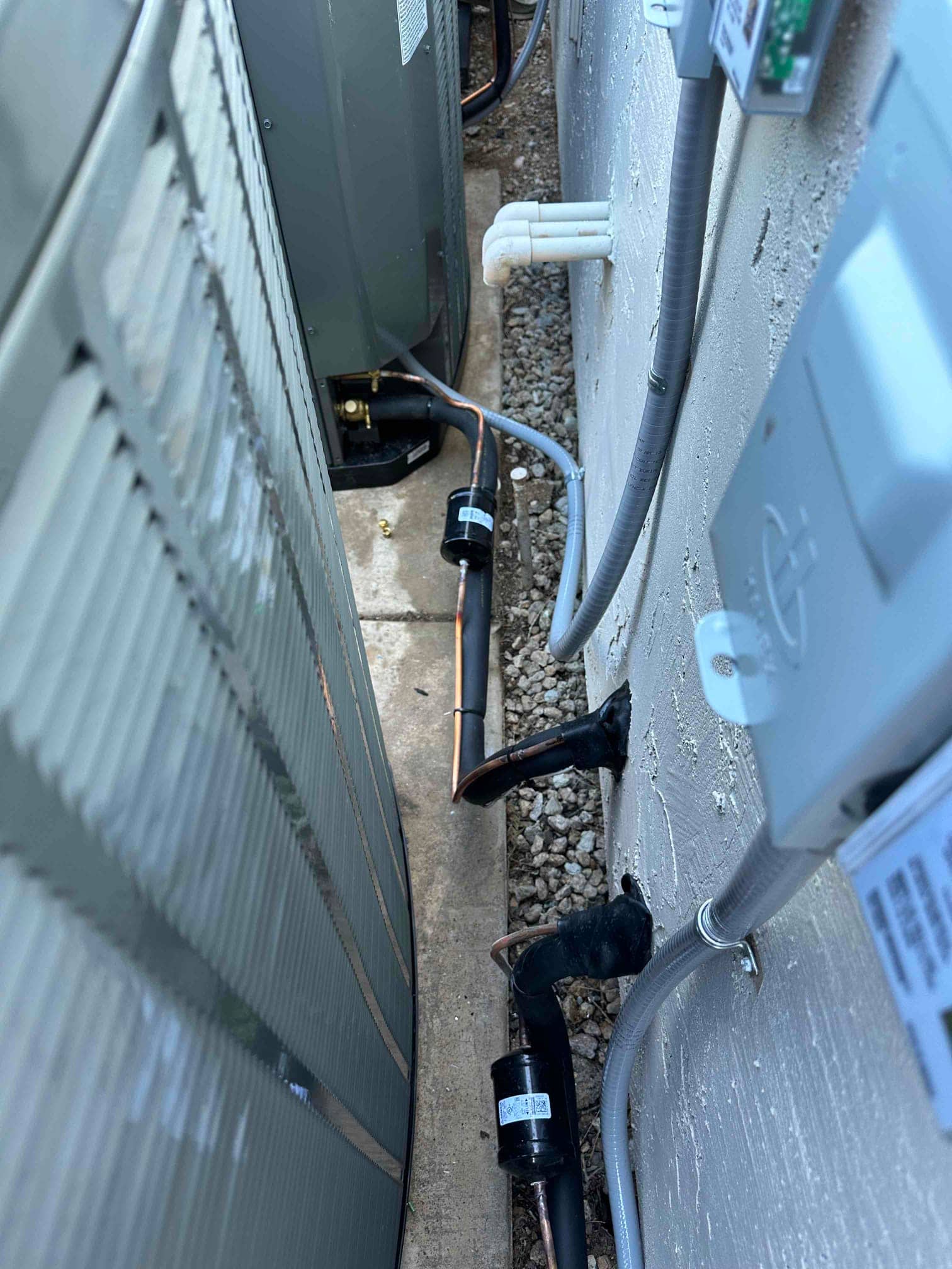 New outdoor condenser set on a pad with insulated refrigerant lines, filter-driers, sealed wall penetrations, and electrical whip to the disconnect.