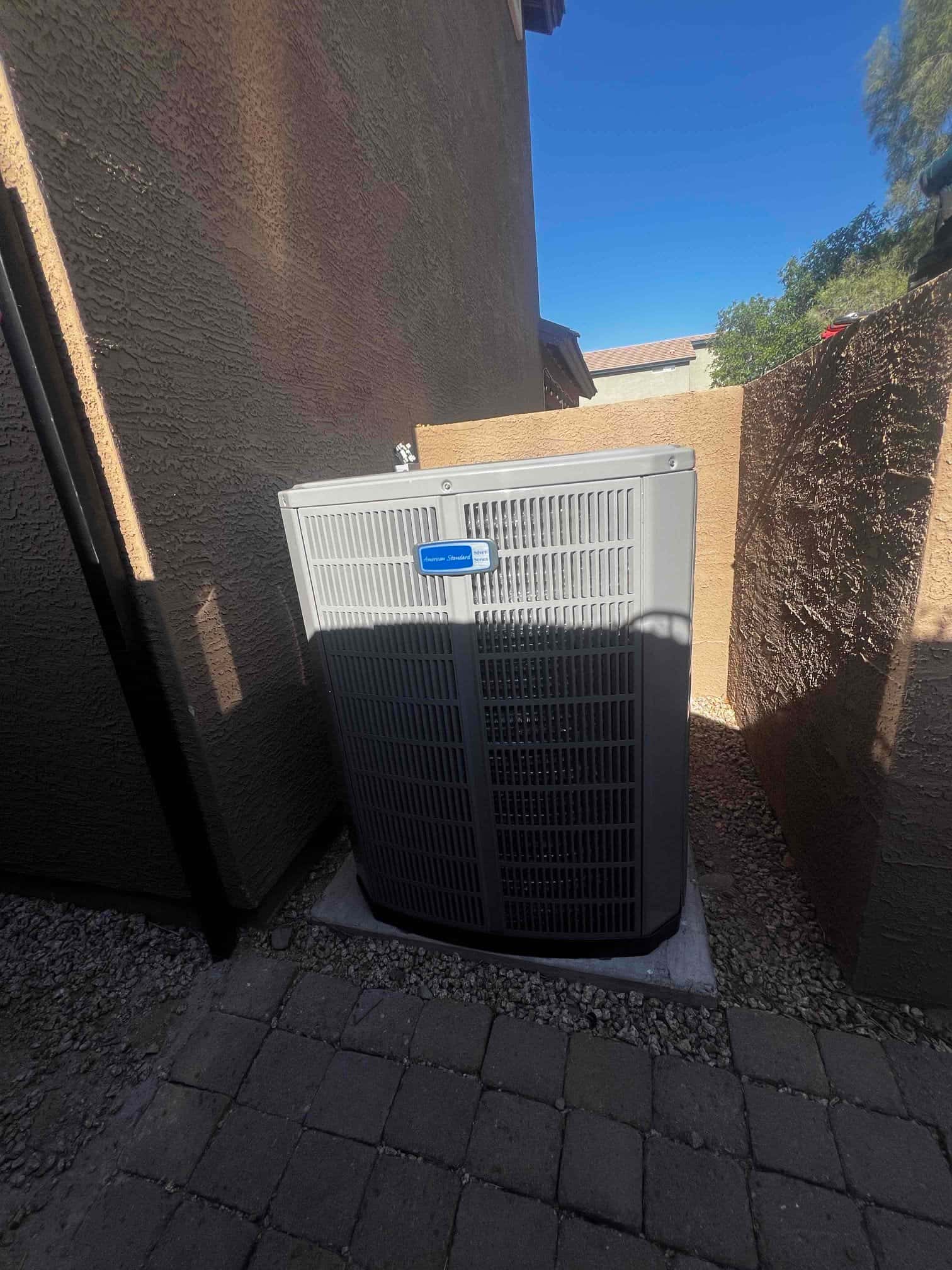 New outdoor heat pump condenser set on a level pad with proper clearances between stucco walls in the side yard.