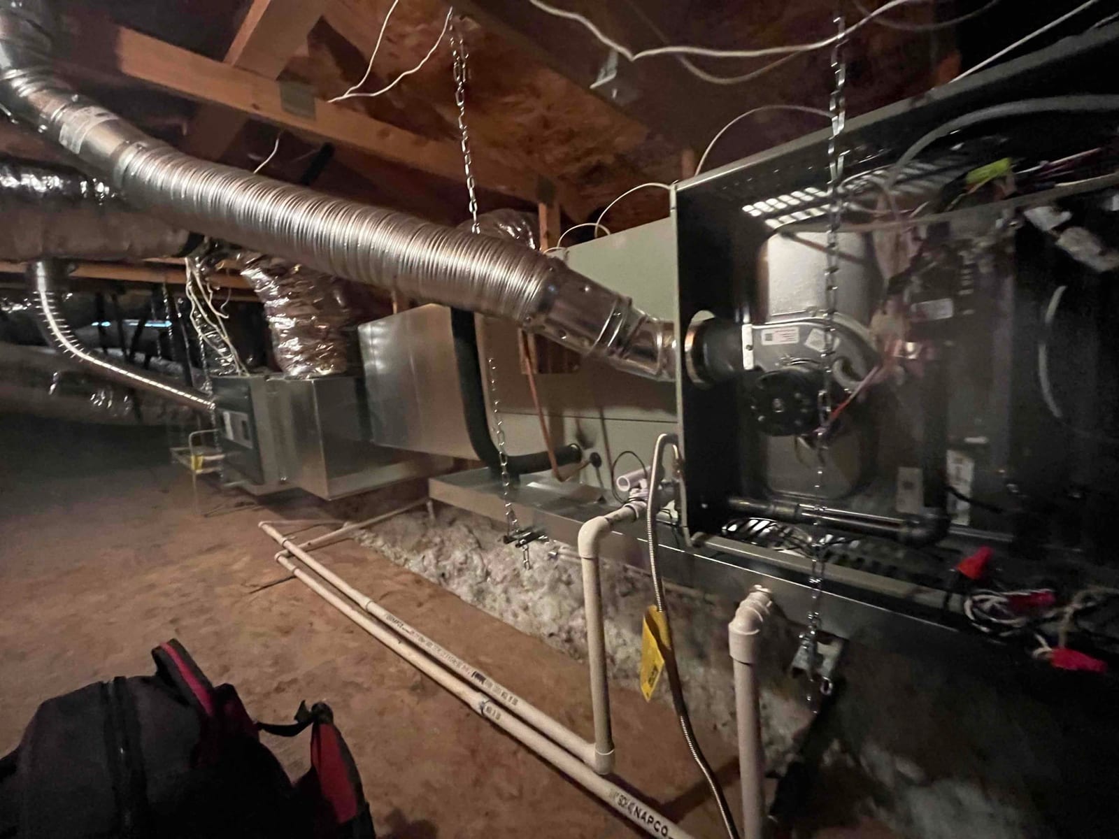New suspended furnace and ductwork installed in attic with condensate drain piping, flexible gas vent, and electrical connections visible.