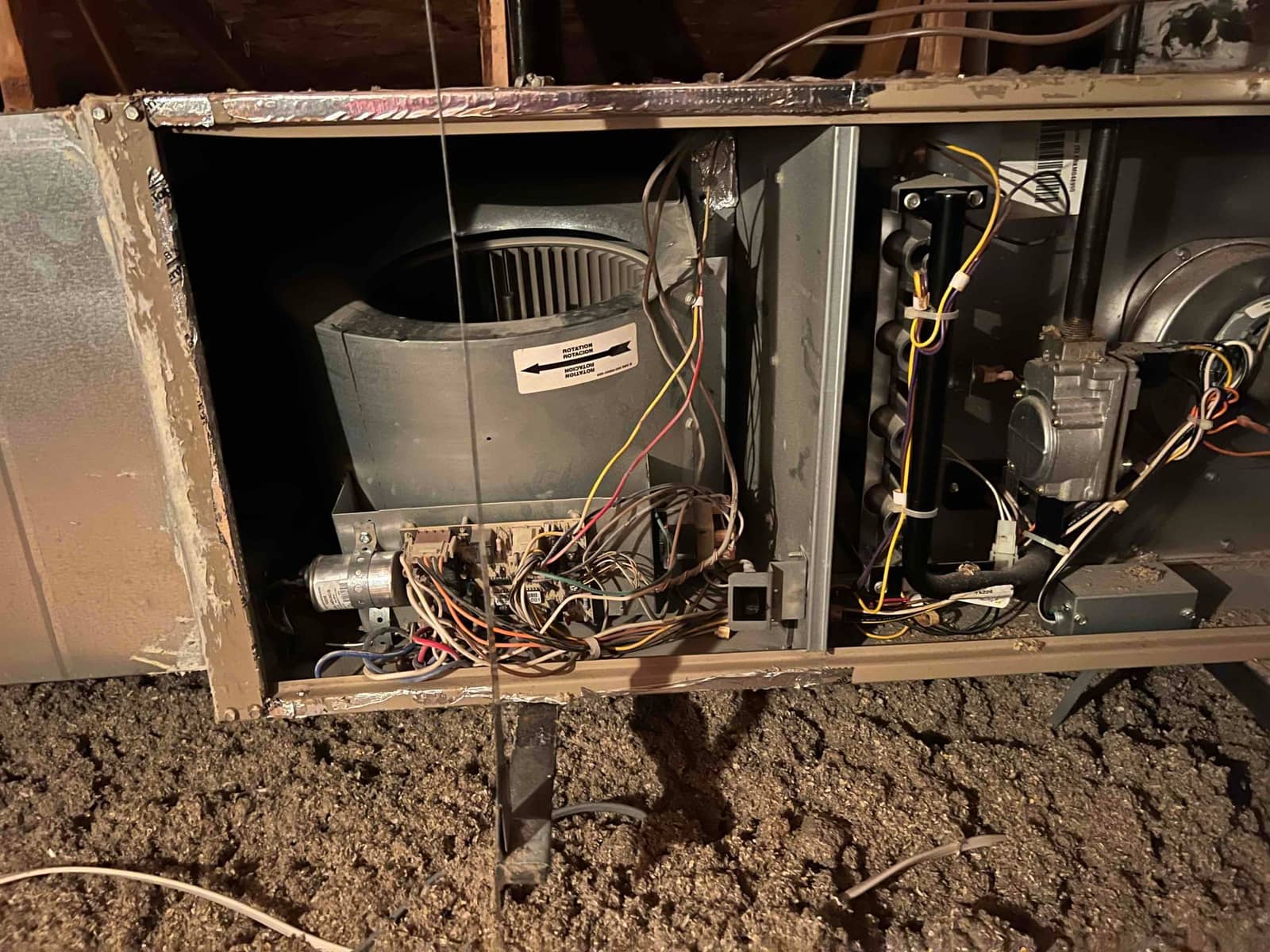 Open horizontal furnace cabinet showing blower assembly, control board wiring, gas valve, and draft inducer, surrounded by loose-fill insulation.