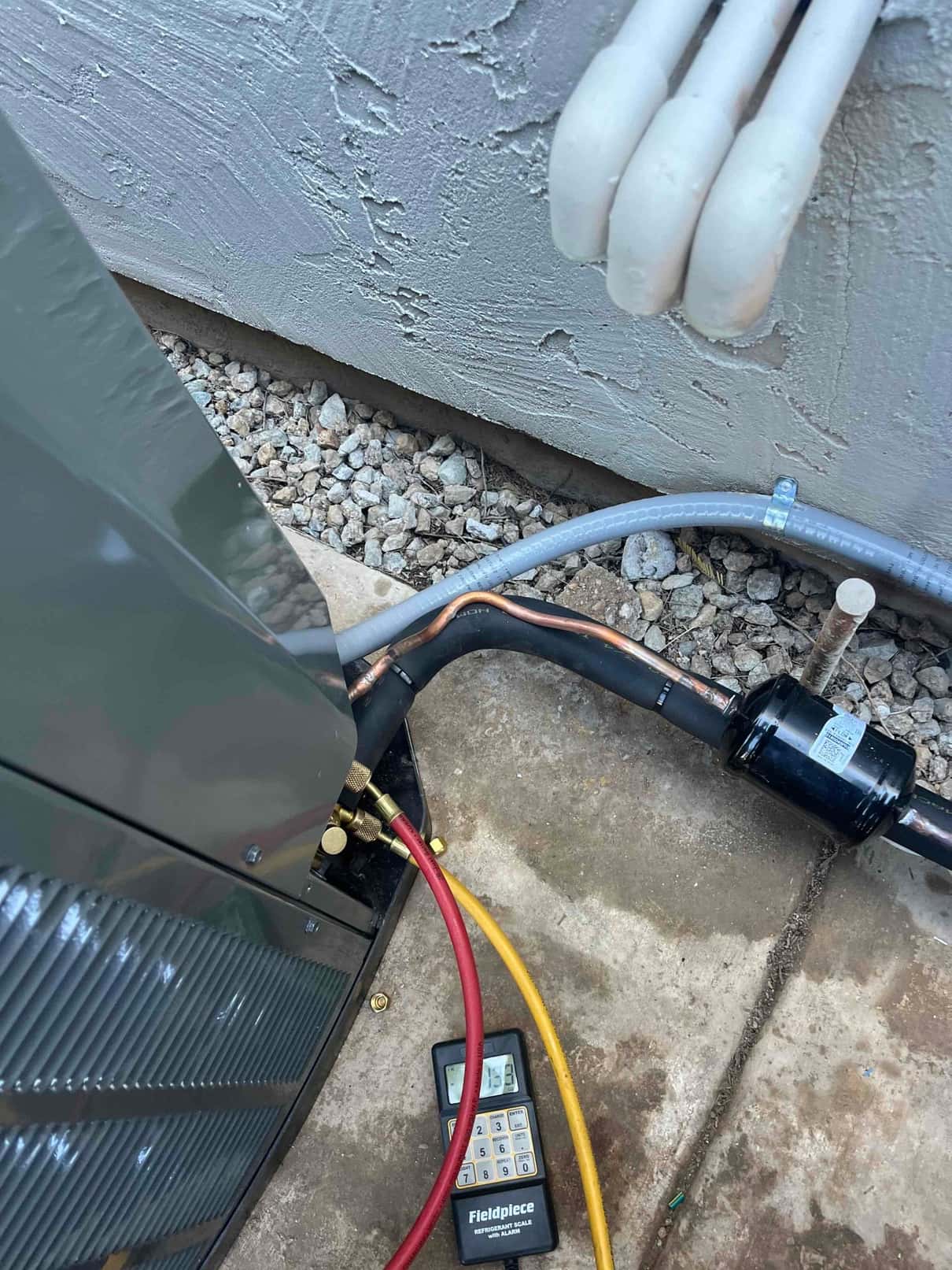 Outdoor condenser connections with brazed copper lines, insulated suction line, liquid-line filter-drier, and hoses attached near the service valves.