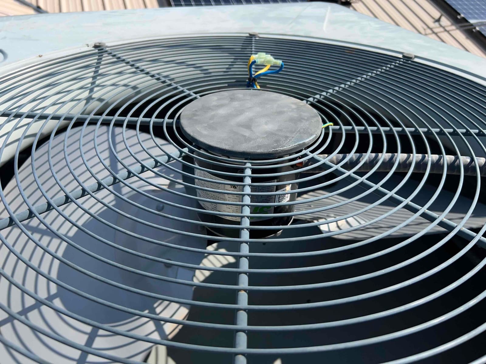 Outdoor condenser fan top with protective grille and central hub, clean condition under bright daylight on the unit.