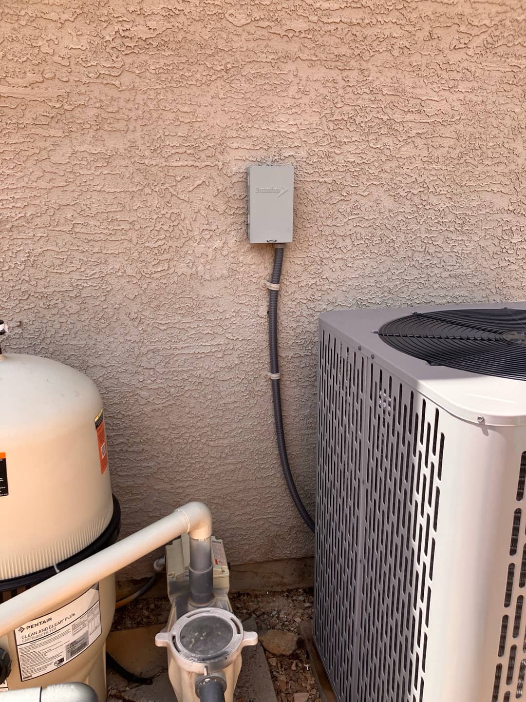 Outdoor condenser set beside a wall with weatherproof electrical disconnect and flexible conduit neatly secured.