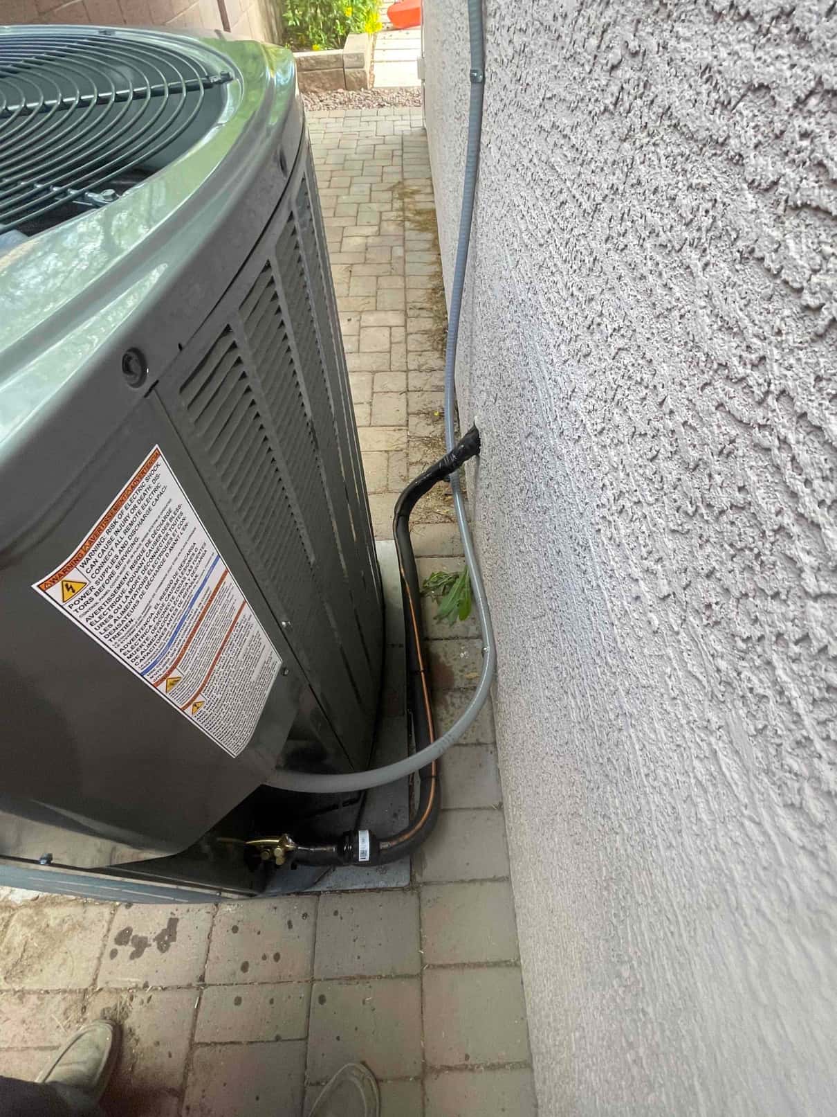 Outdoor condenser set on a level pad with insulated refrigerant lines and electrical whip routed into the wall penetration.