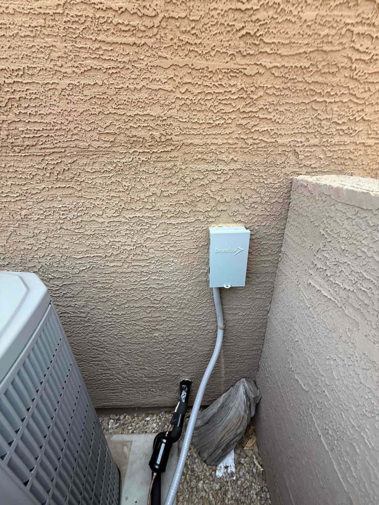 Outdoor condenser set on a pad with insulated refrigerant line and newly installed weatherproof electrical disconnect on the wall.