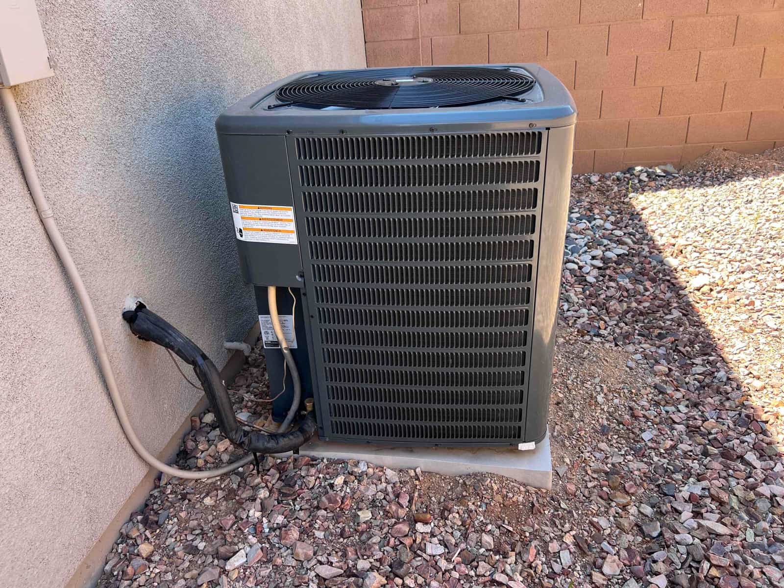 Outdoor condenser unit on pad beside house wall, with torn refrigerant line insulation and connected electrical conduit.
