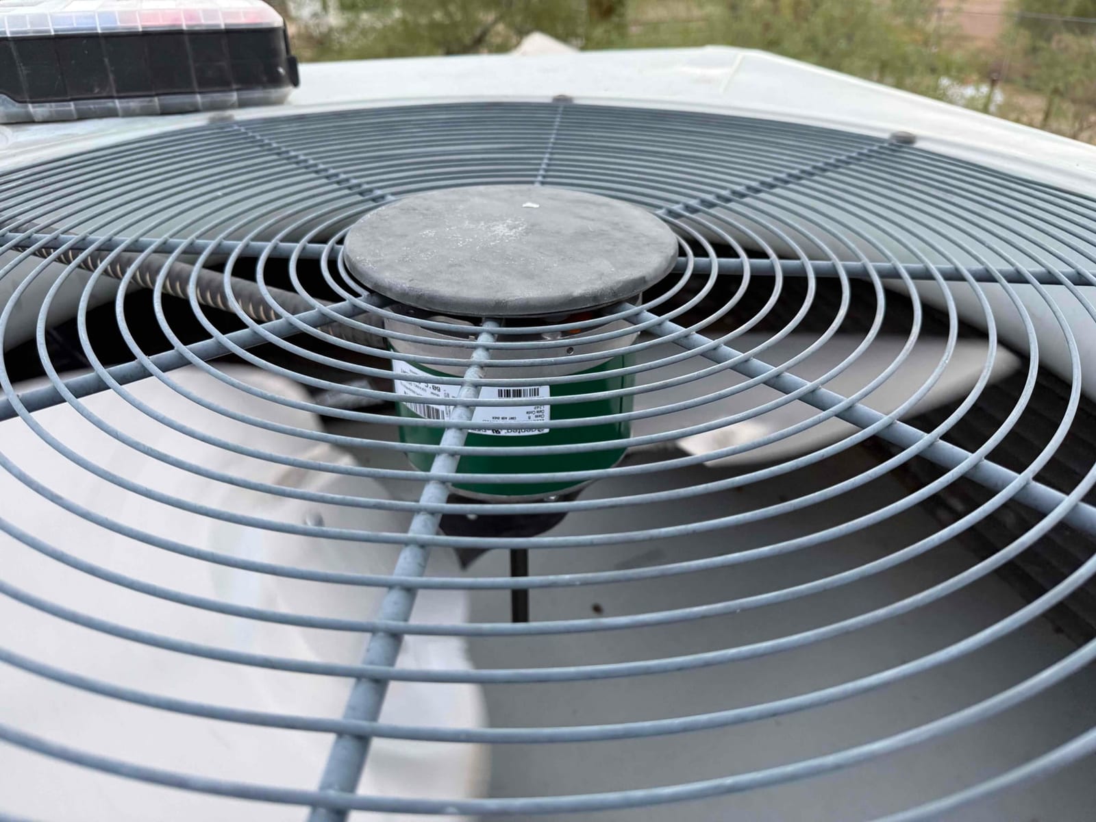 Outdoor condenser unit with protective fan grille, showing the condenser fan motor housing centered beneath the top cover.