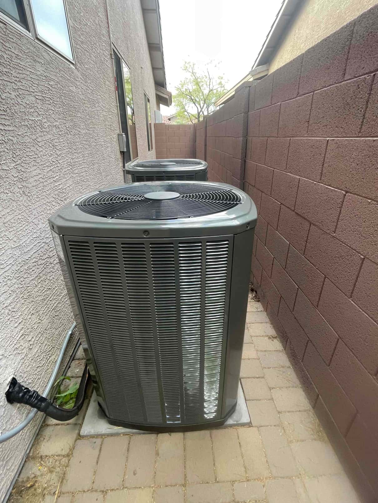 Two outdoor condensers set on level pads along the side yard with insulated line sets routed into the wall.