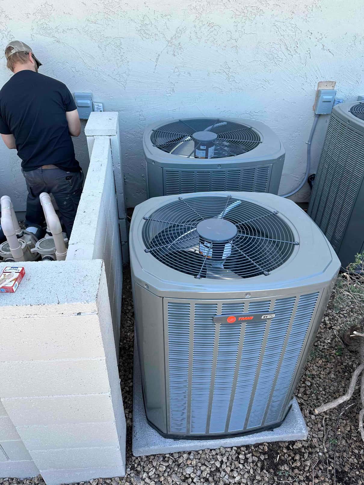 Two outdoor condensers set on level pads with electrical disconnects mounted on the wall as a technician works nearby.