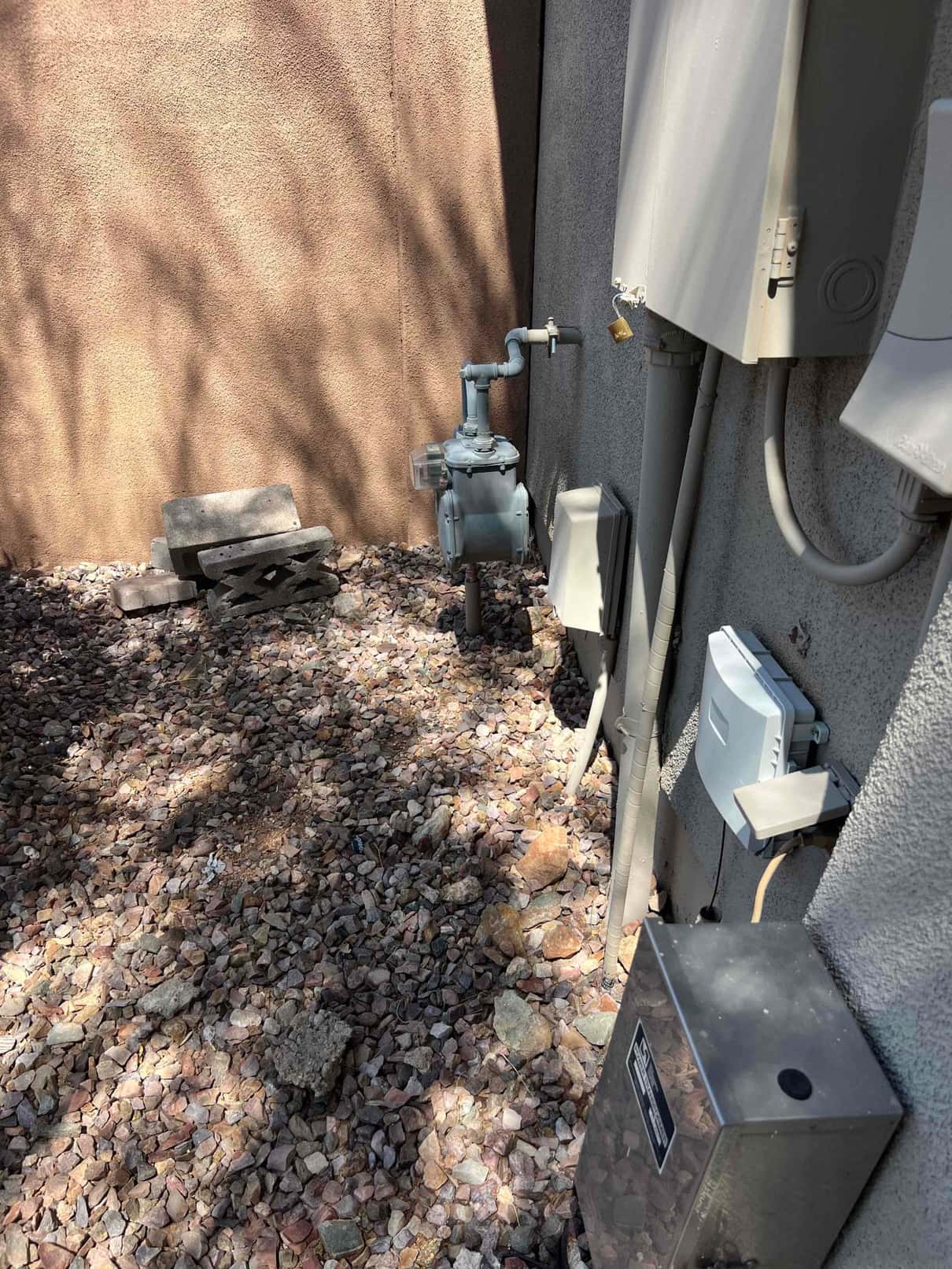Outdoor electrical disconnect boxes and conduit mounted on the exterior wall beside a residential gas meter.