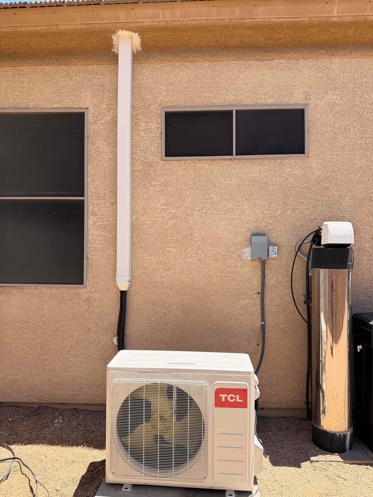 Outdoor mini-split condenser set on a pad with line-set cover up the wall and weatherproof electrical disconnect installed.