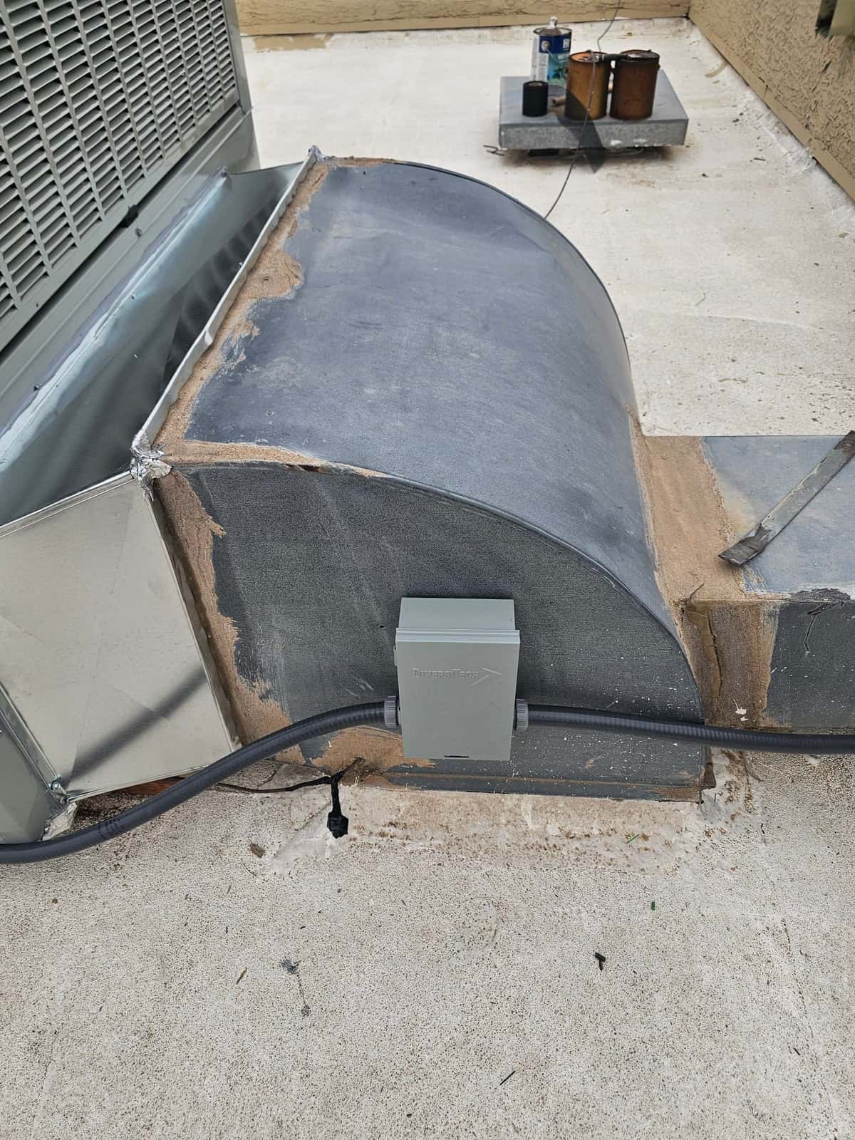 Outdoor unit connected to roof curb ductwork with sealed transitions and a mounted weatherproof electrical disconnect in flexible conduit.