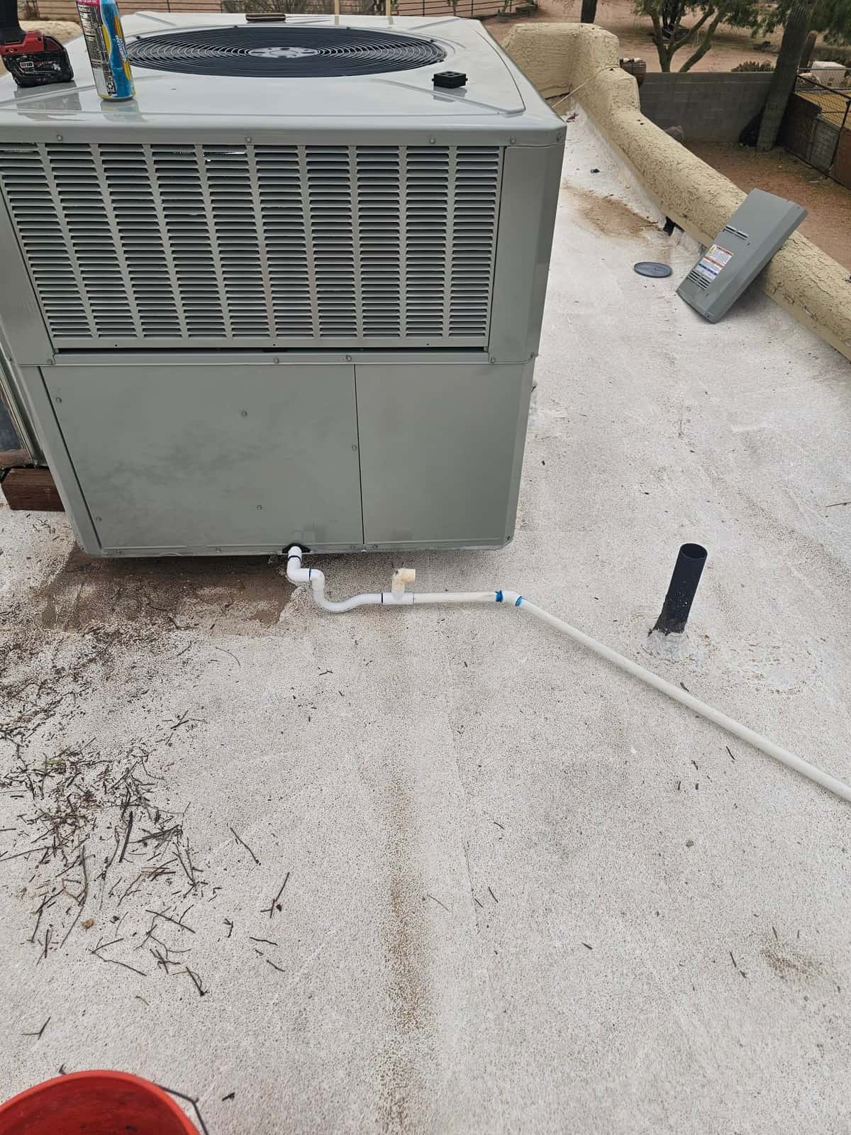 Package heat pump set on rooftop with newly routed PVC condensate drain, clean termination, and sealed roof penetration.