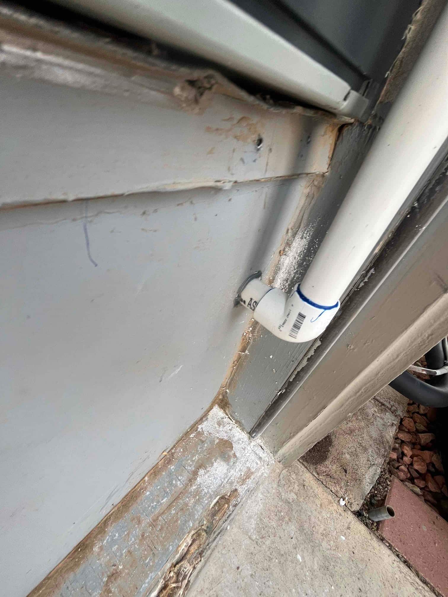 PVC condensate drain penetrates the exterior wall with sealed caulking at the siding and foundation joint.