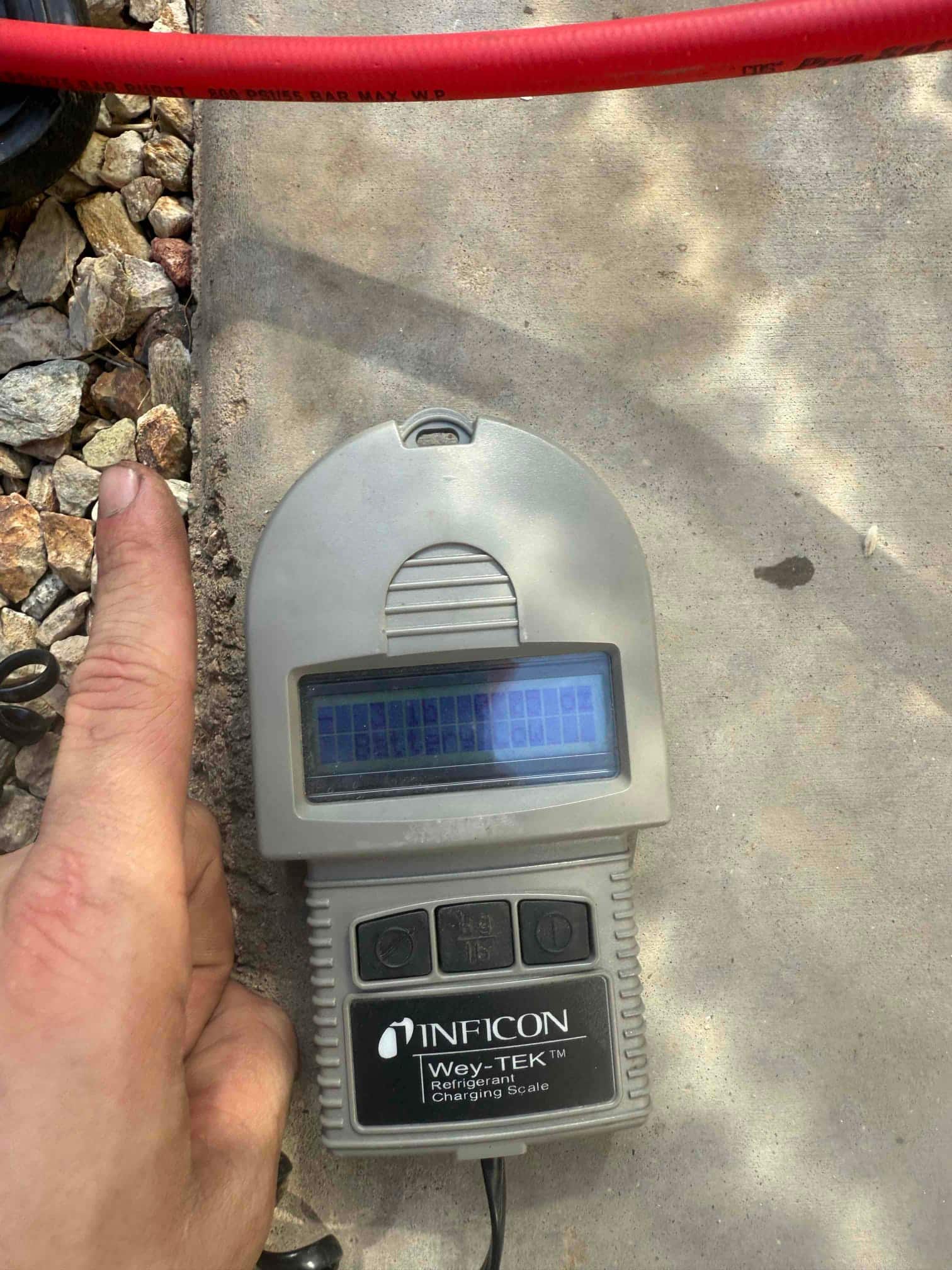 Refrigerant charging scale on the ground next to a red hose during HVAC installation work.