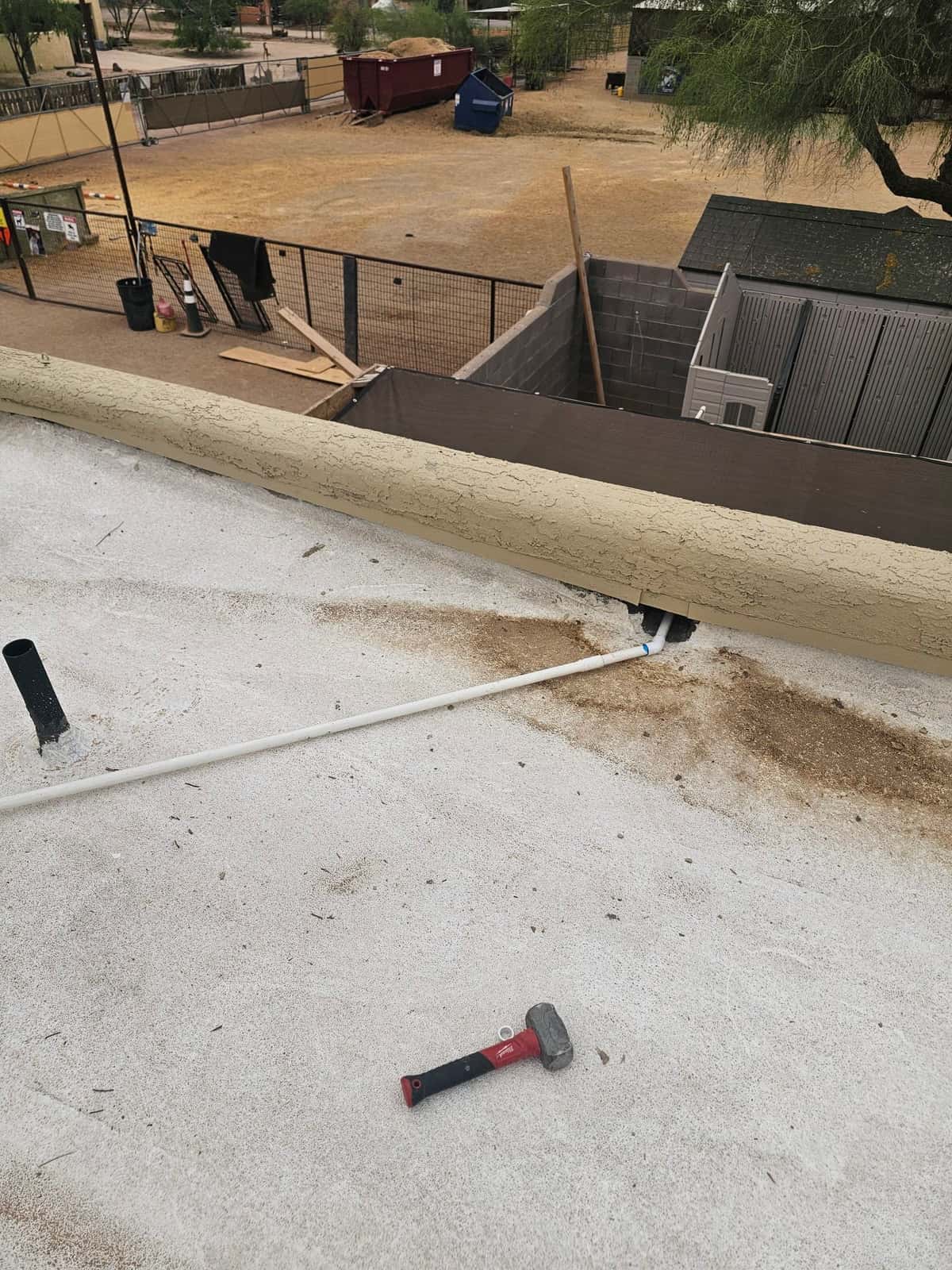 Rooftop installation detail showing new PVC condensate drain routed to the parapet with roof penetrations and tools nearby.