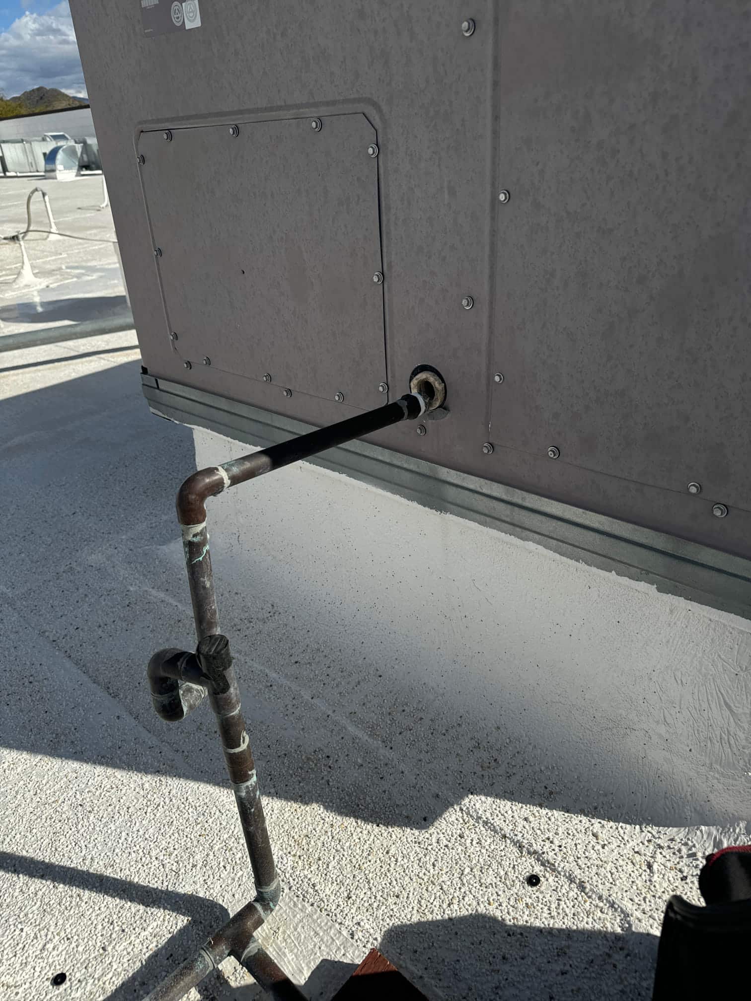 Rooftop package unit’s condensate drain line enters the cabinet, showing exterior piping with corrosion and roof-mounted routing.