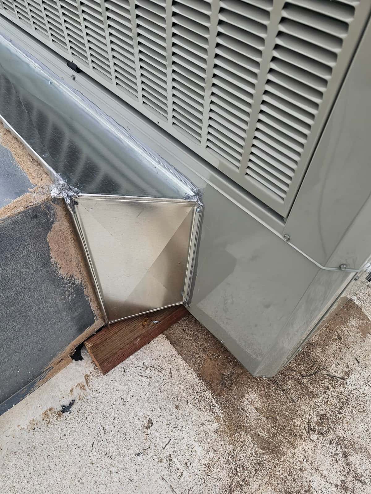 Sheet metal transition duct sealed to the side of a packaged HVAC unit, showing clean metalwork and secured connections at the base.