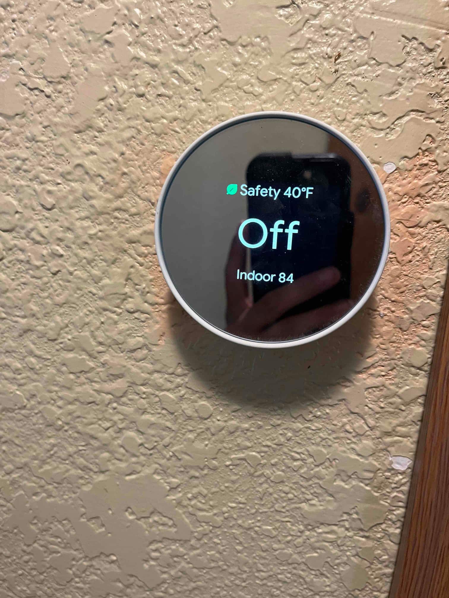 Smart thermostat on a textured wall displays system Off, Safety 40°F active, and Indoor 84.