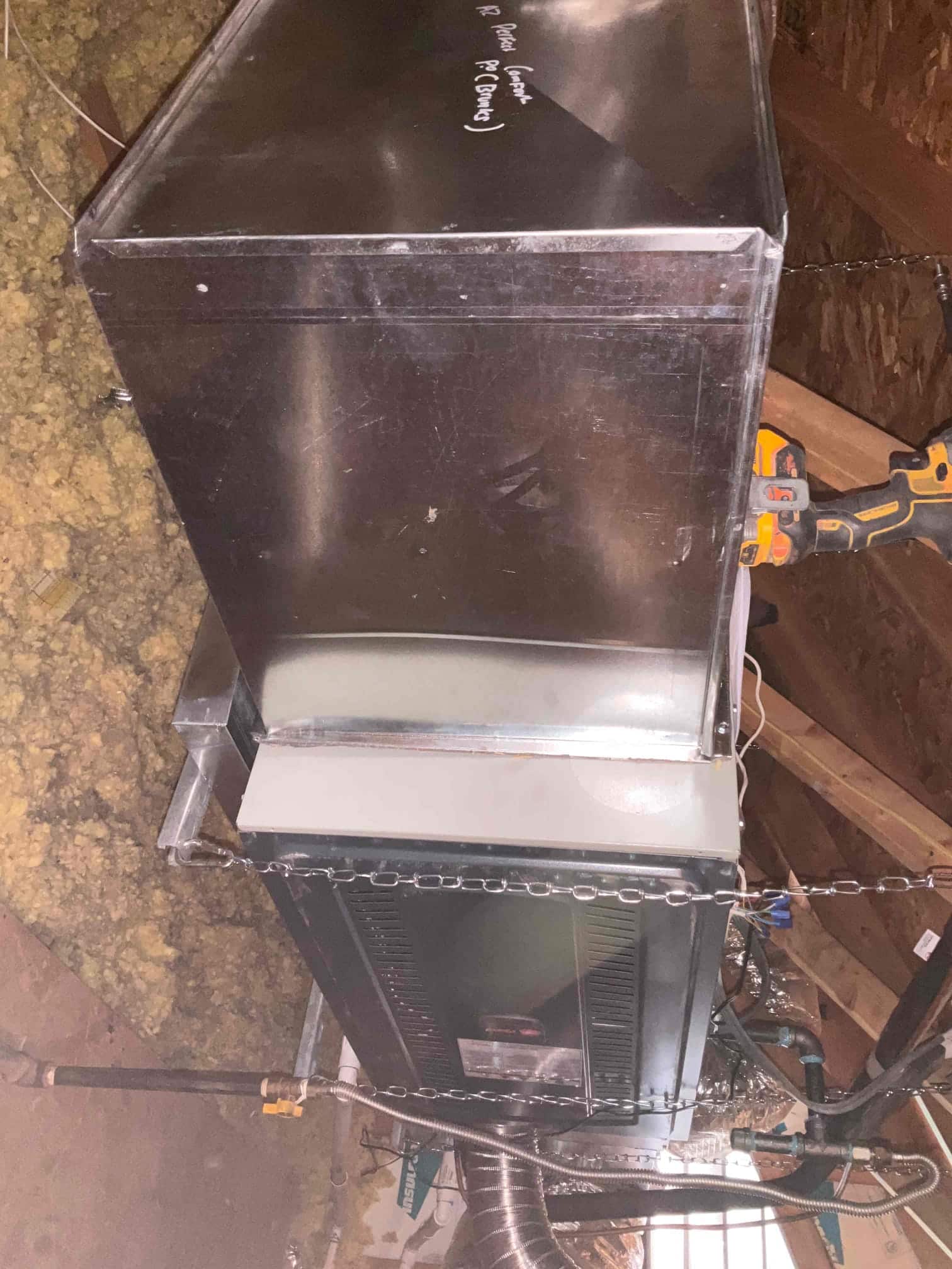 Suspended air handler installed in attic with sheet metal plenum, insulated flex duct connections, and supporting chains visible.