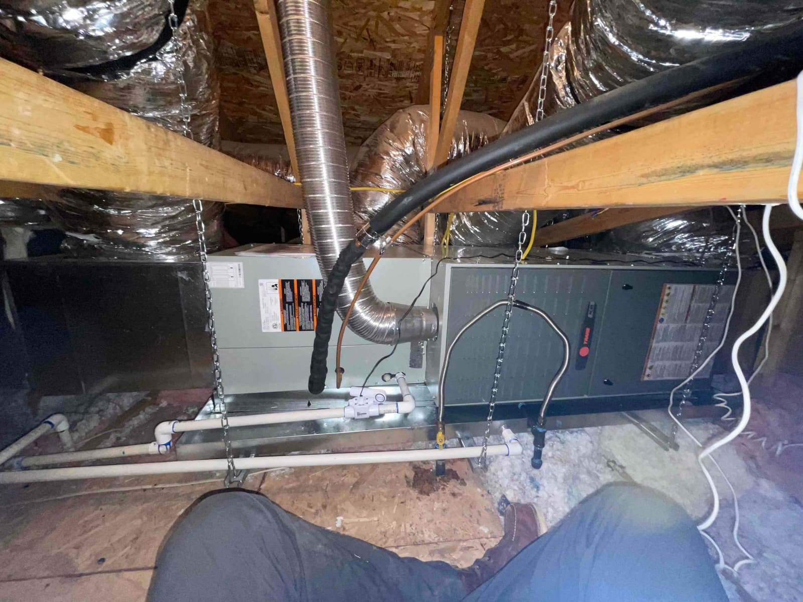 Suspended attic air handler and furnace installation with insulated ducts, condensate drain piping, and refrigerant lines secured and supported.