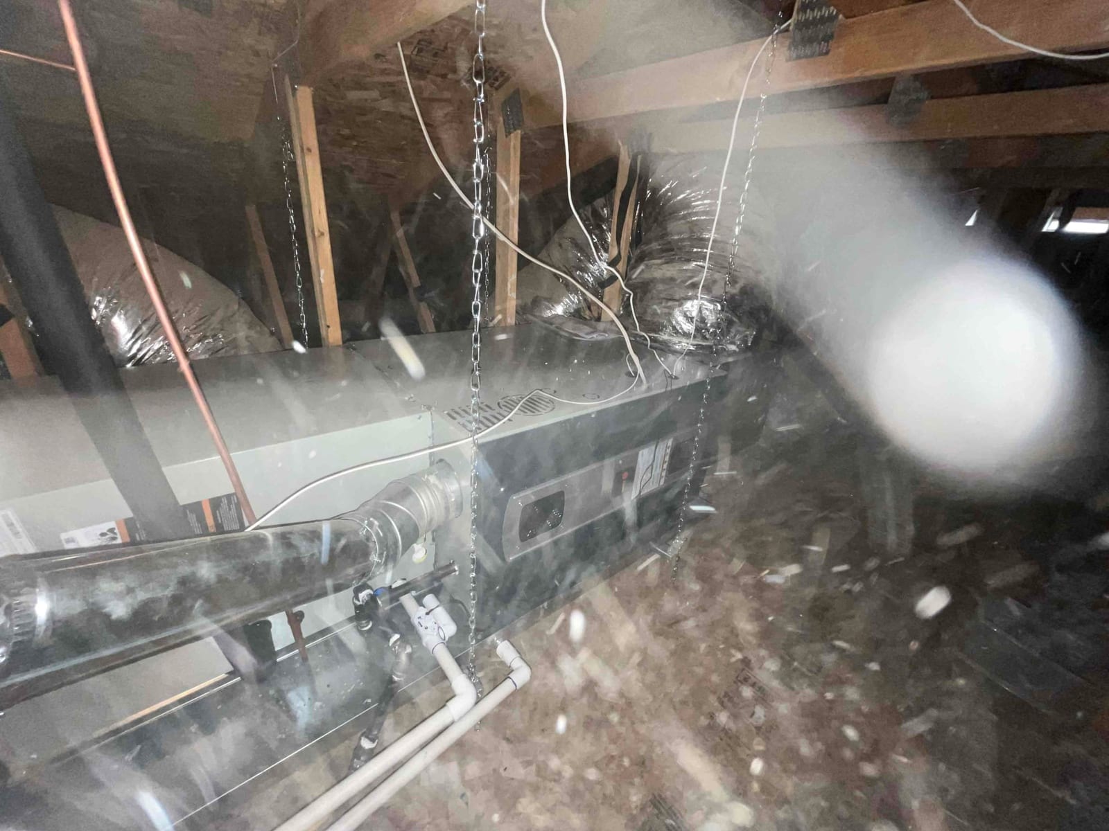 Suspended attic air handler with insulated duct connections, condensate drain piping, and venting installed and supported by hanging chains.
