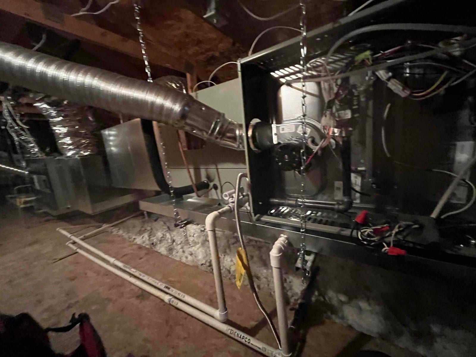 Suspended attic furnace and coil assembly with connected ductwork, condensate drains, and wiring visible during installation.