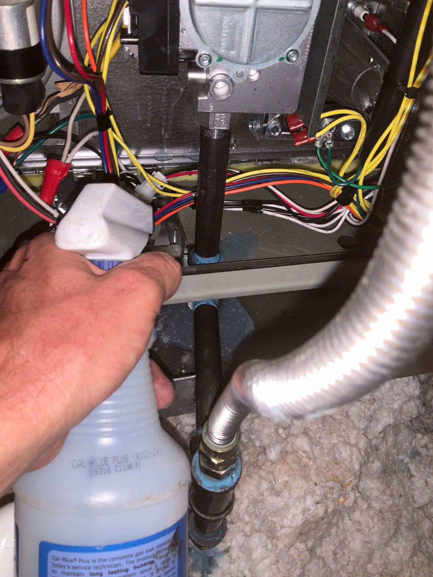 Technician applies leak detection solution to gas piping connections inside the furnace compartment, inspecting joints near wiring and controls.