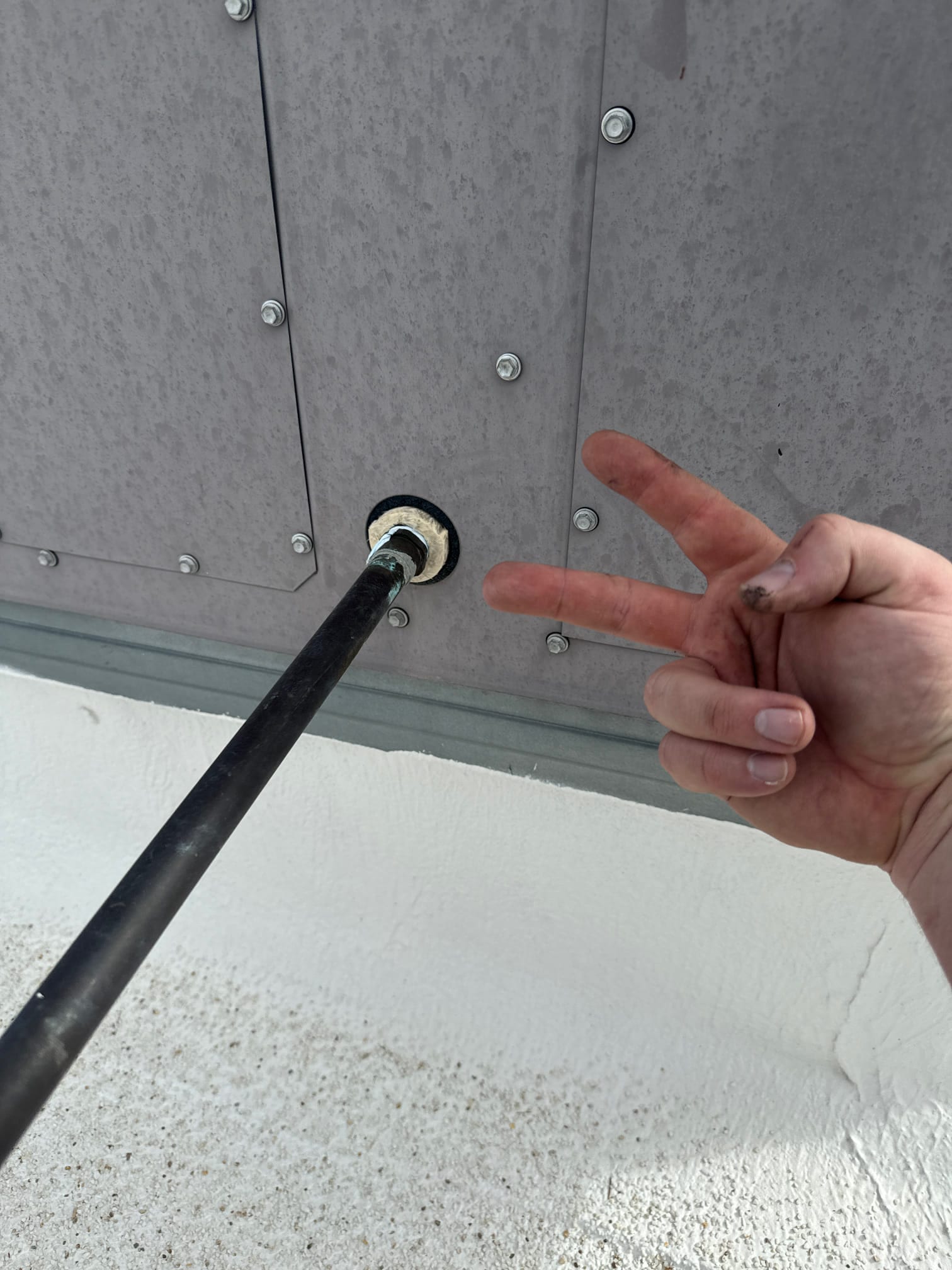 Technician’s hand holds a condensate drain line inserted through a sealed wall penetration with fresh sealant around the grommet.