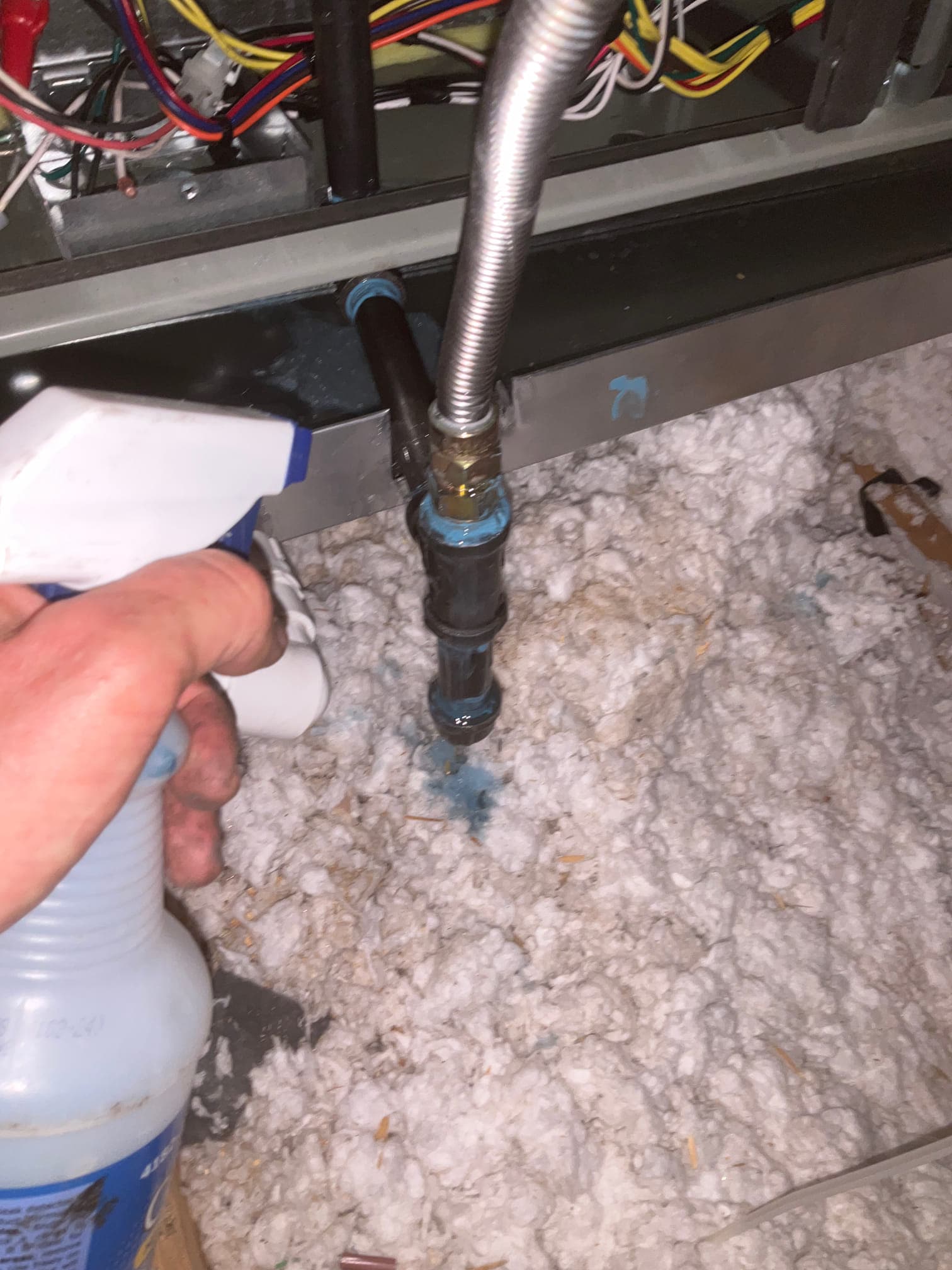 Technician sprays leak detector on new condensate drain and flexible water connection at the air handler during installation.