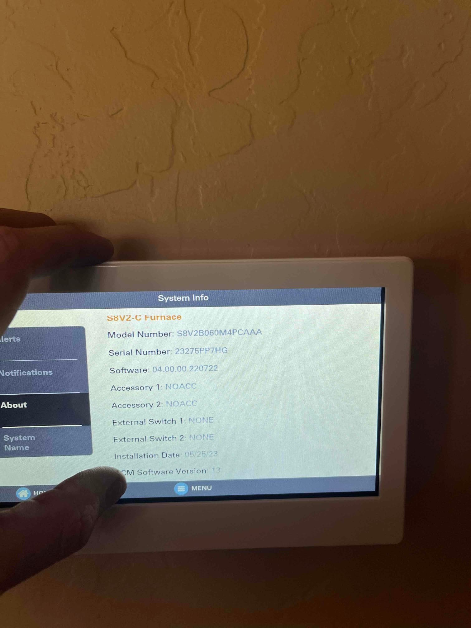 Thermostat touchscreen displays system information for the furnace while a technician holds the frame during setup.
