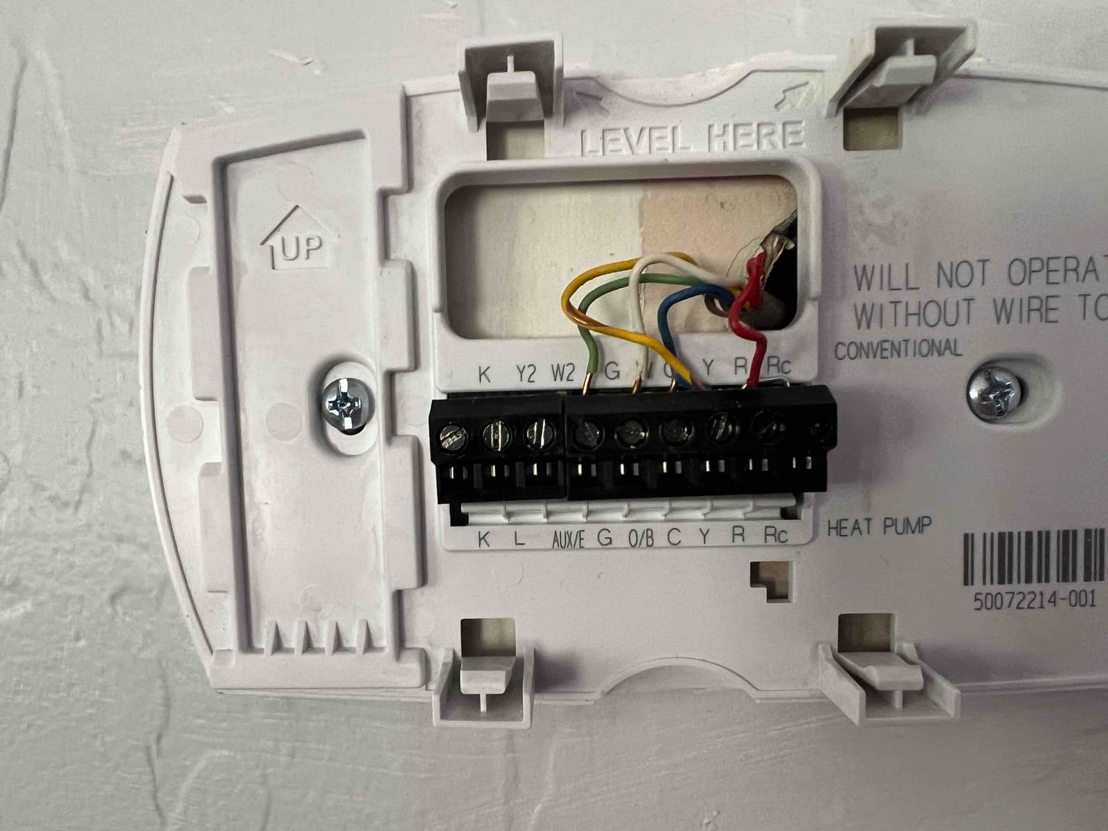 Thermostat wall plate showing low-voltage conductors landed on G, Y, W2/Aux, R, and C terminals, with heat pump labeling visible.