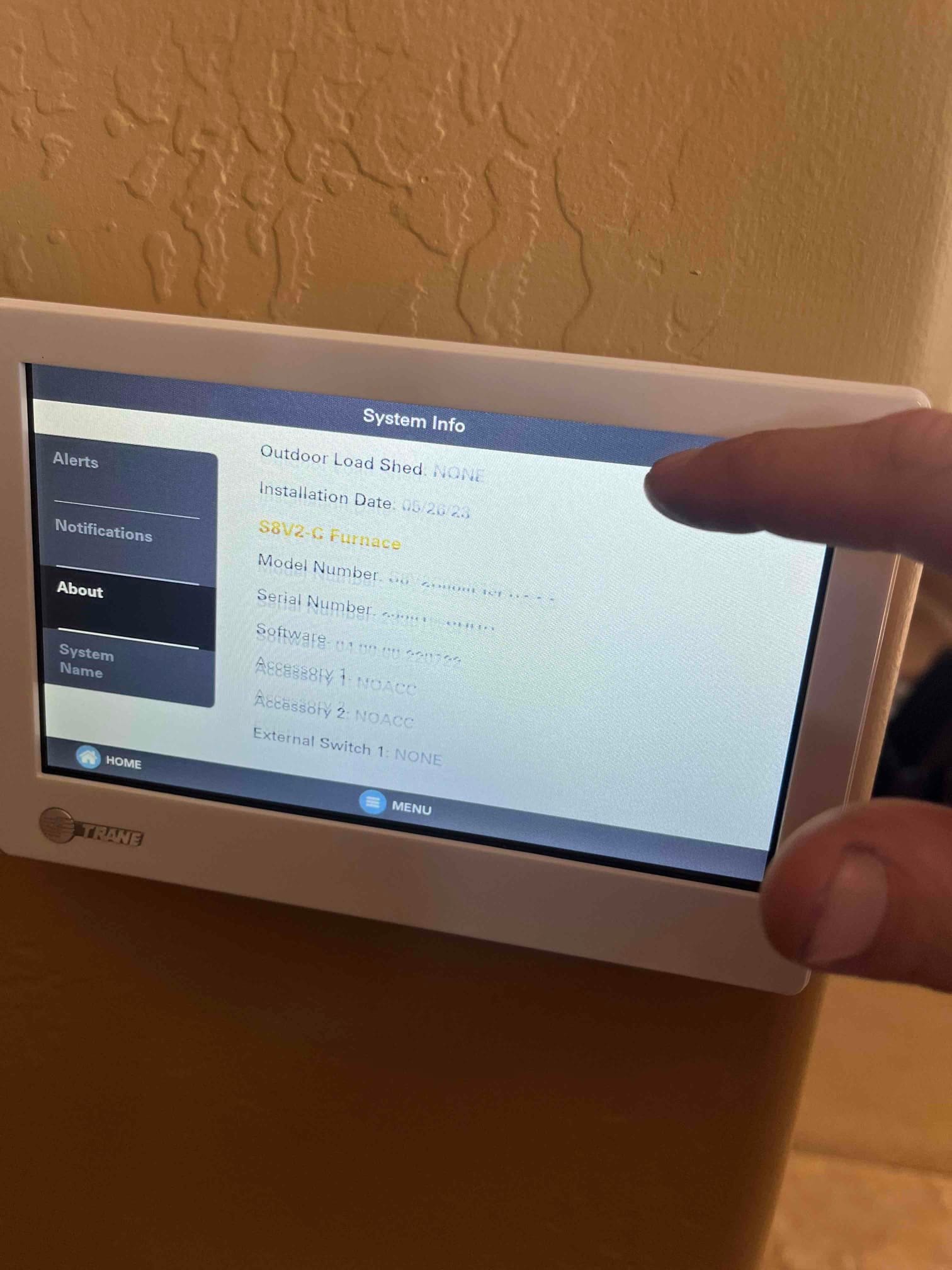 Touchscreen thermostat displays system info menu while a technician interacts with the interface during commissioning setup.