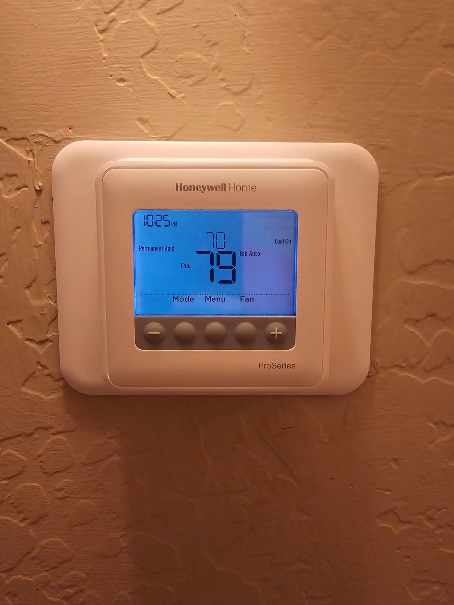 Wall-mounted digital thermostat illuminated and set to cool mode with fan on auto and temperature displayed.