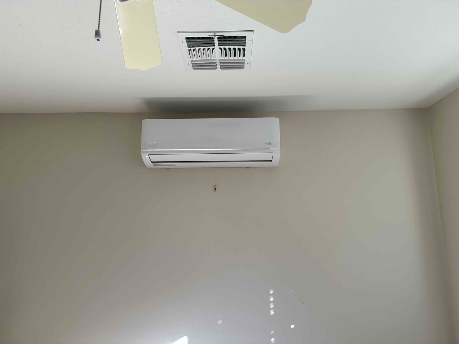 Wall-mounted mini-split indoor unit installed on a finished wall beneath a ceiling supply grille and fan.