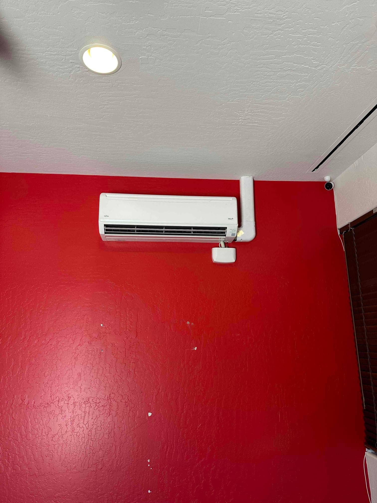 Wall-mounted mini-split indoor unit installed with line-set cover and condensate drain neatly routed along the red interior wall.
