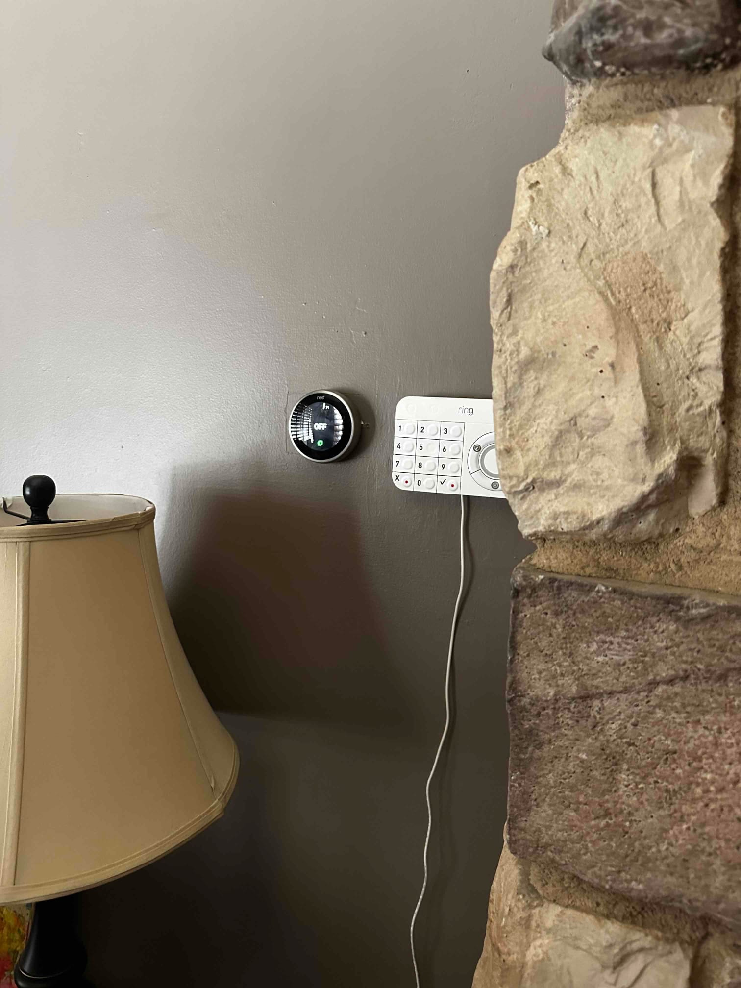 Wall-mounted smart thermostat and security keypad installed beside a stone fireplace, showing an indoor temperature display.