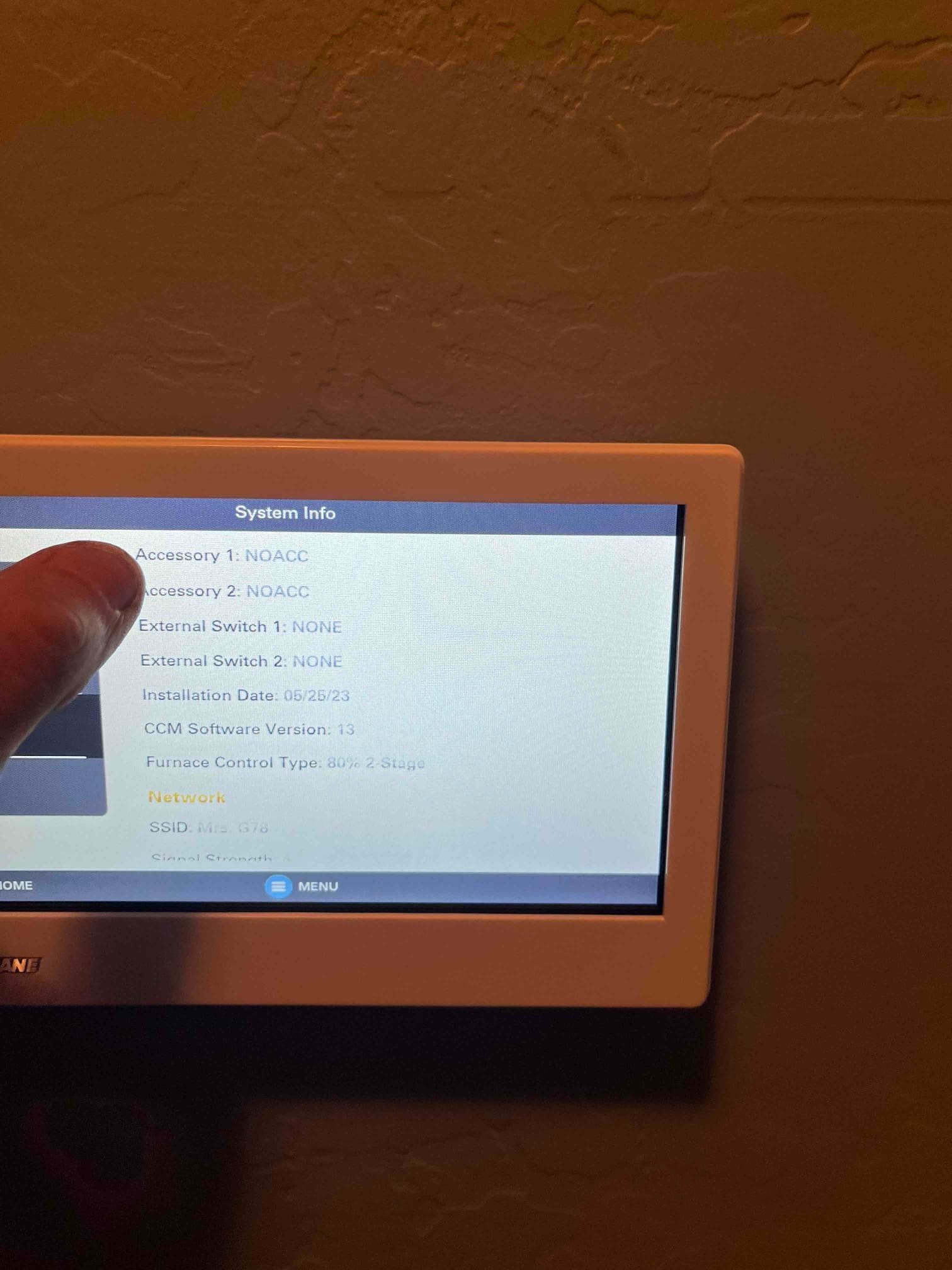 Wall-mounted thermostat displays system information and network settings during setup after installation.