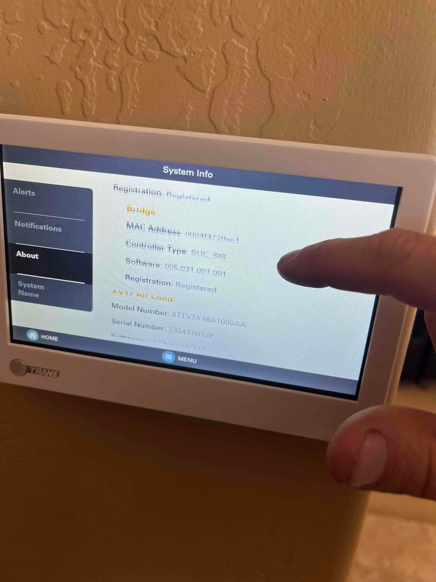 Wall-mounted touchscreen thermostat displays system information while being operated during setup and commissioning.