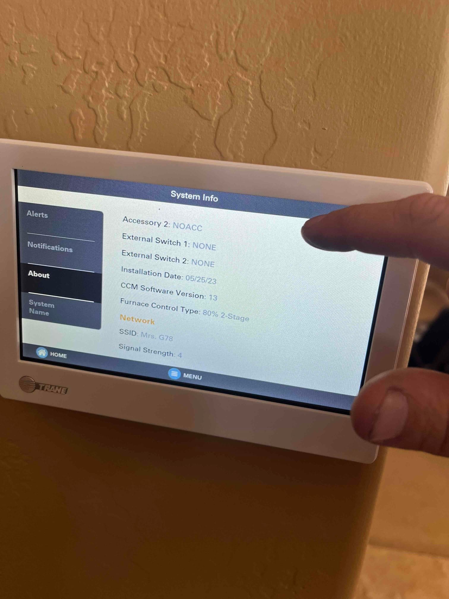 Wall-mounted touchscreen thermostat displays system information during setup, with a technician’s hand interacting with the interface.