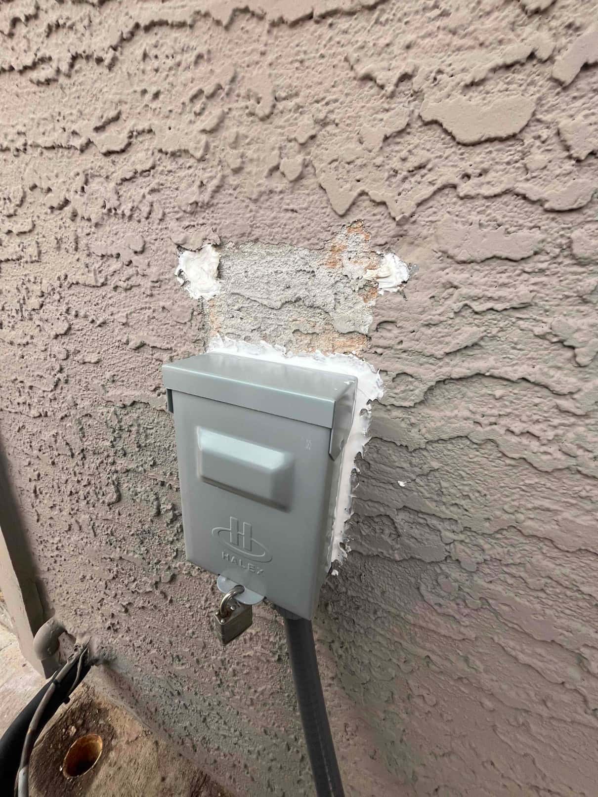 Weatherproof HVAC disconnect box mounted on exterior wall with sealed penetration and flexible conduit routed to the condenser.