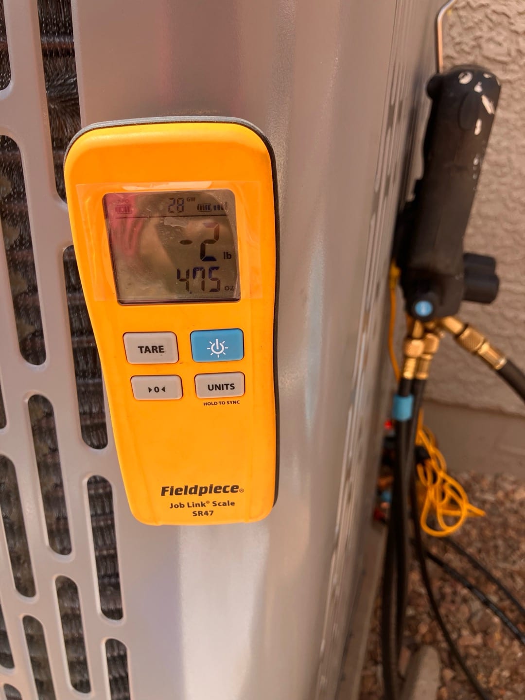 Wireless refrigerant scale attached at the outdoor condenser shows a charge change of 2 lb 4.75 oz during commissioning.