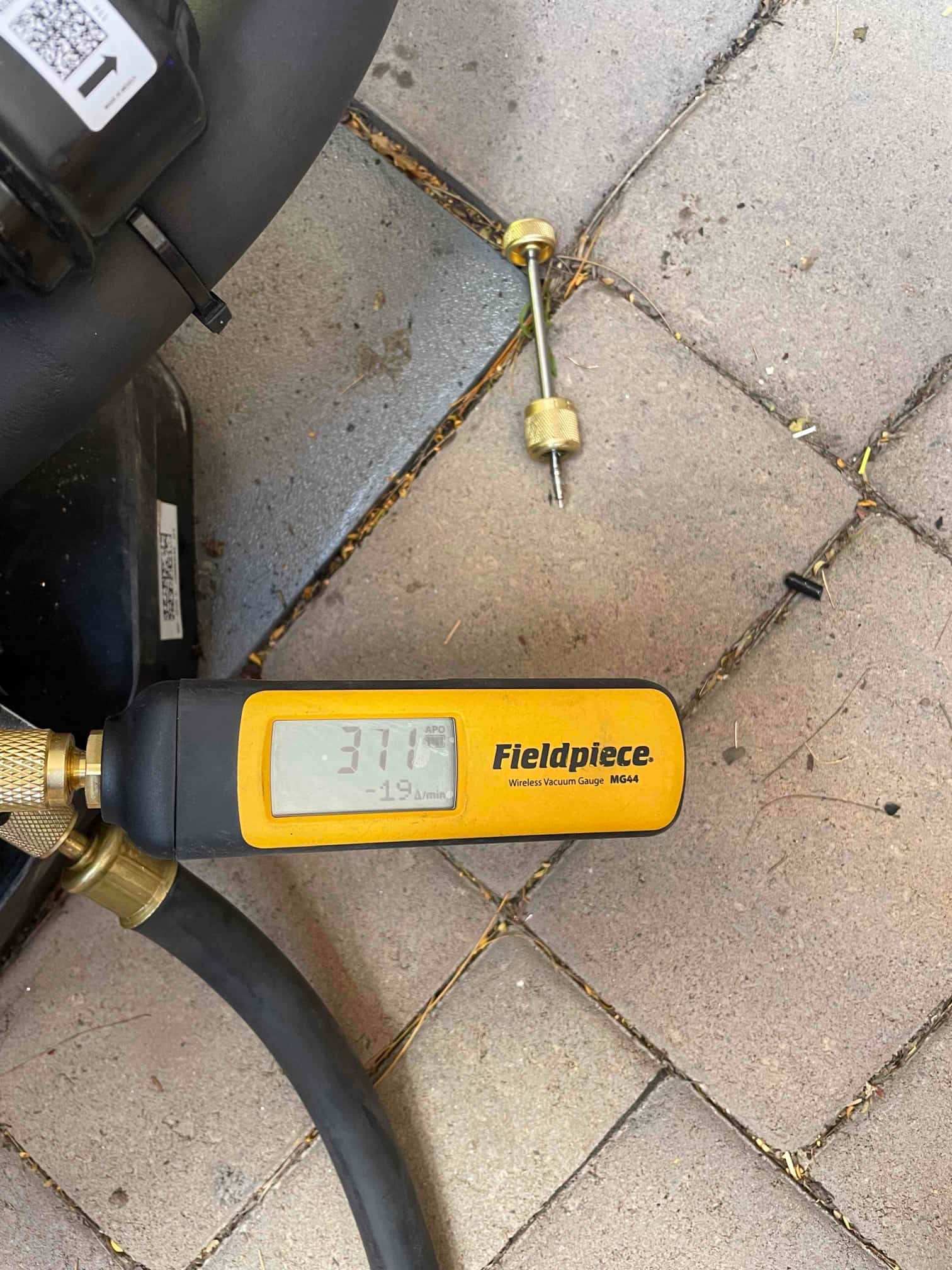 Wireless vacuum gauge connected to the system shows 371 microns during evacuation, verifying a deep vacuum before charging.