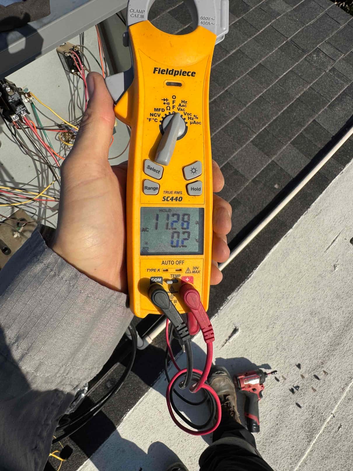 Clamp meter displays 12.9 A while clamped around a single conductor at the outdoor condenser.