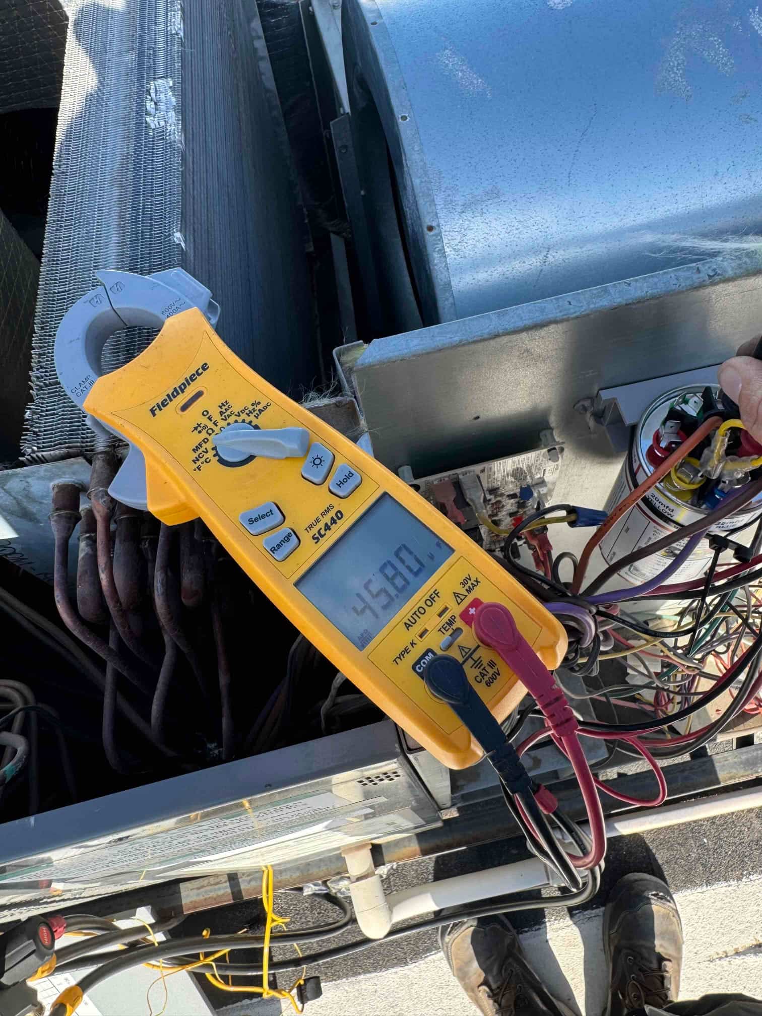 Clamp meter measures 45.80 μF on the capacitor at the outdoor condenser wiring during air conditioning repair.