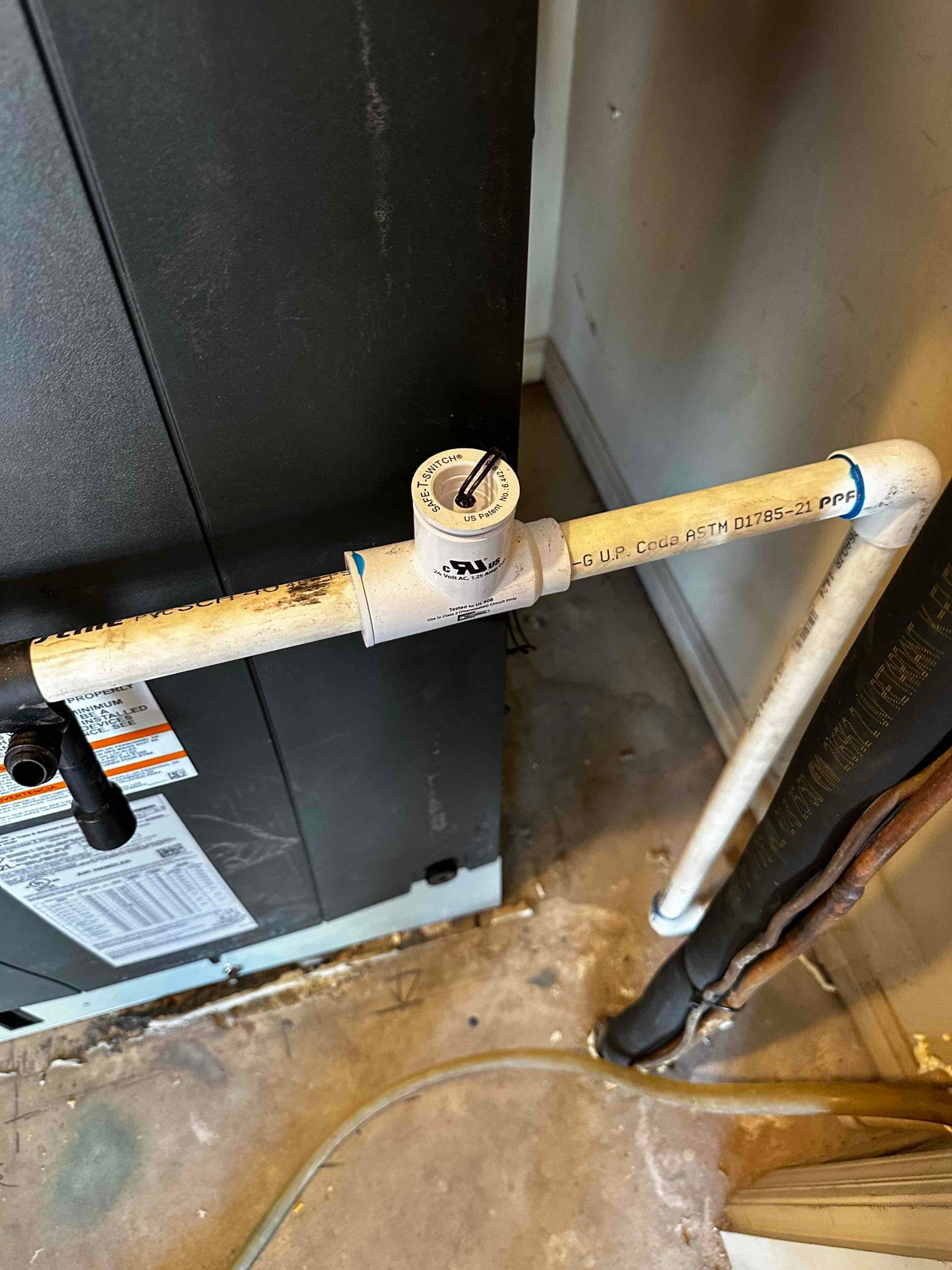 Condensate drain with float safety switch installed beside the indoor air handler, with insulated refrigerant lines routed to the floor penetration.