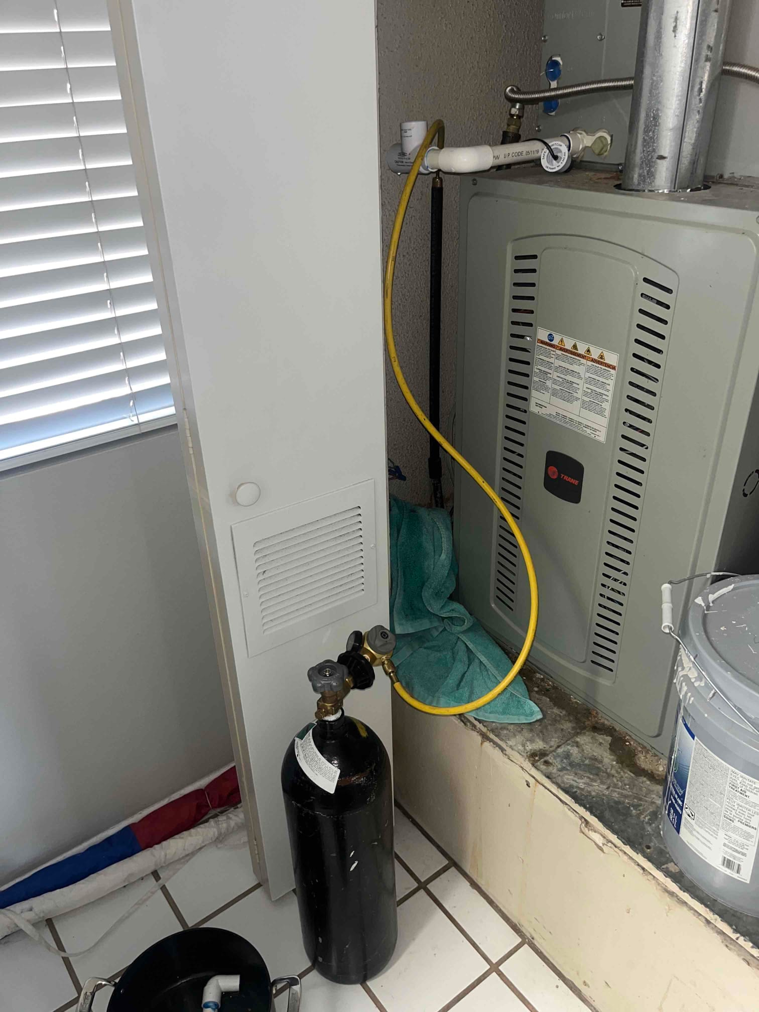 Condensate drain line at the air handler with a yellow hose connected and towels placed to manage drainage during repair.